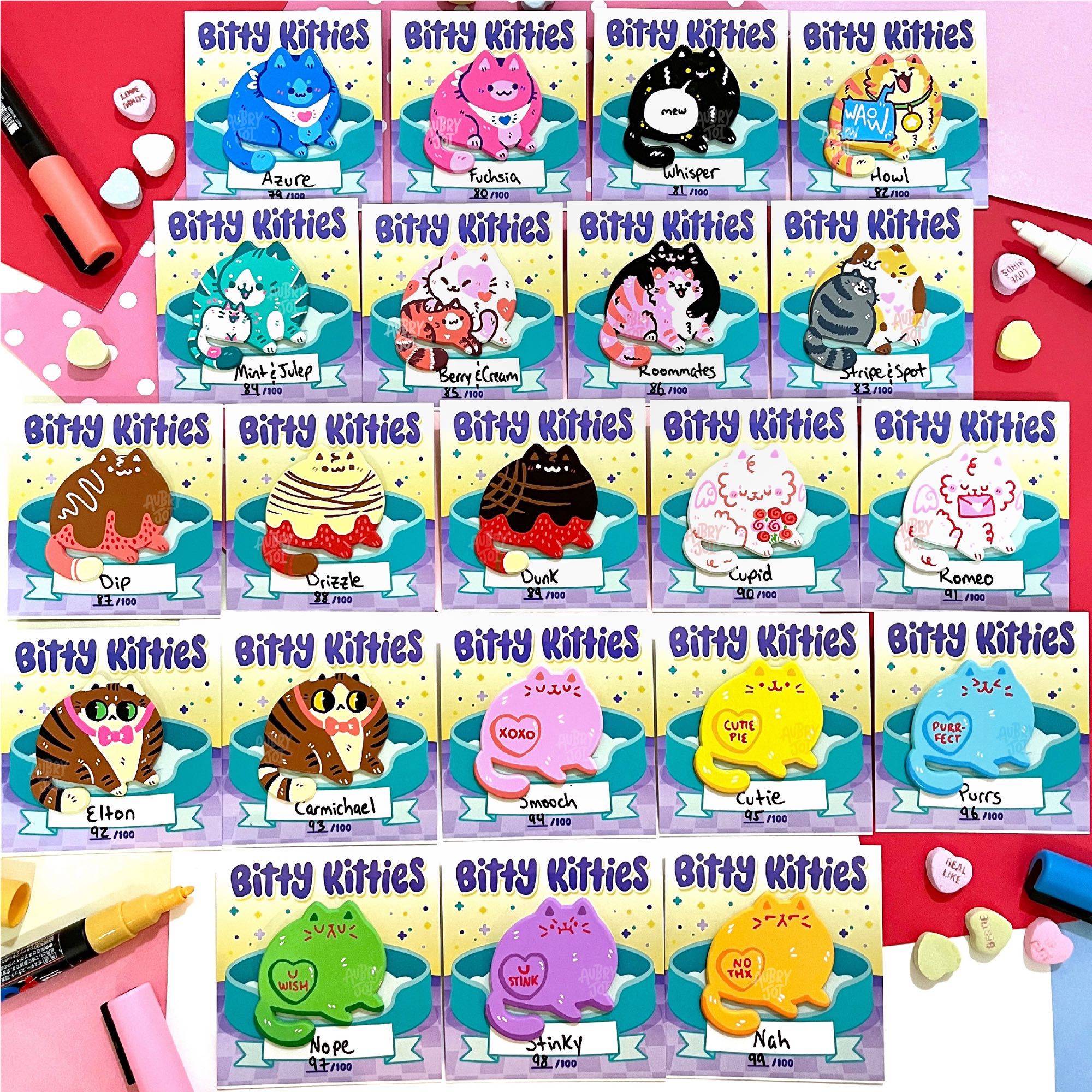 A photo of 21 colorful, hand-painted fat cat enamel pins. Each one is unique. Most are Valentine’s Day themed, in colors like pink, white, red, & brown. Some look like chocolate covered strawberries; others look like conversation heart candies; some are just colorful. Each pin is on a backer card that says “Bitty Kitties” on top, and has a unique name & number at the bottom.