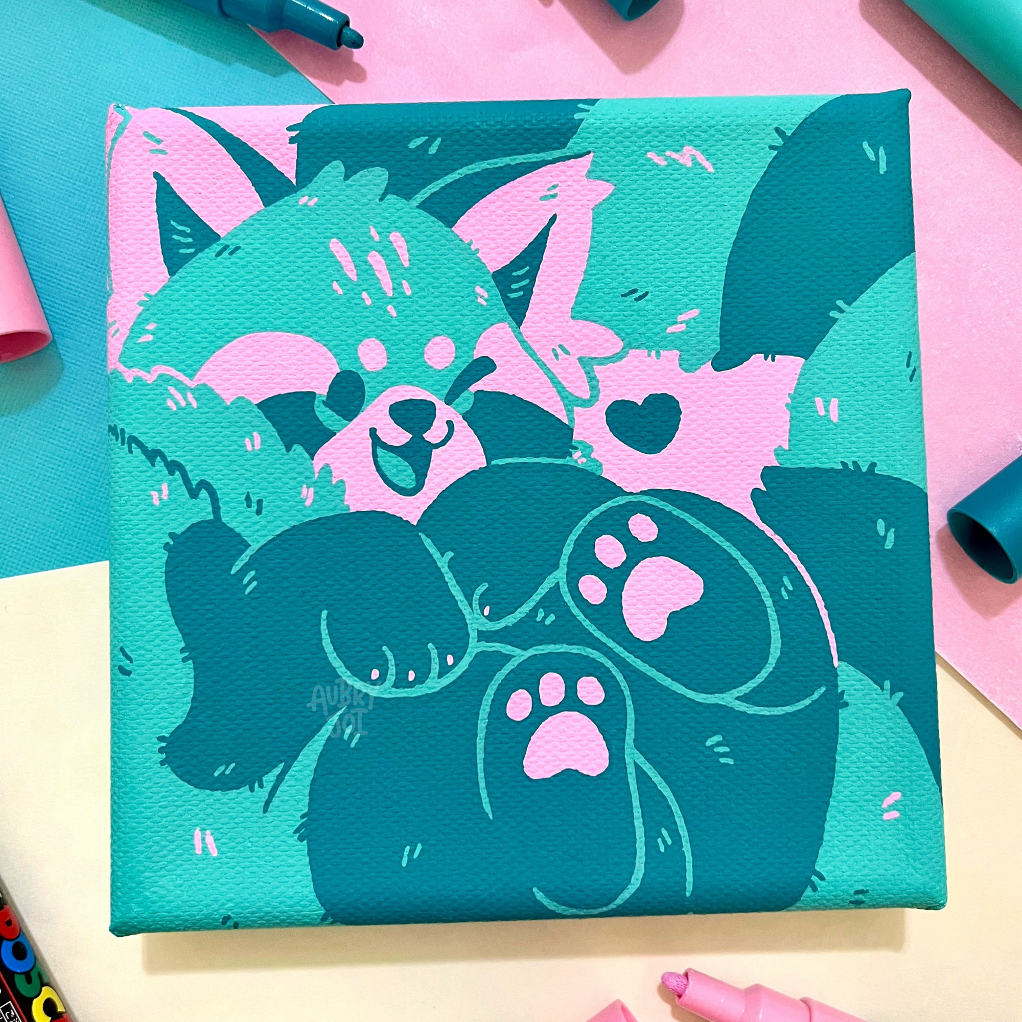 A painting of a teal & pink red panda on a square canvas. The panda is squished into the frame, on its back, with its tail curled up behind it by its head. Its paws are in the air and it’s winking. The colors are bright and graphic. Around the painting are a few scattered Posca pens.