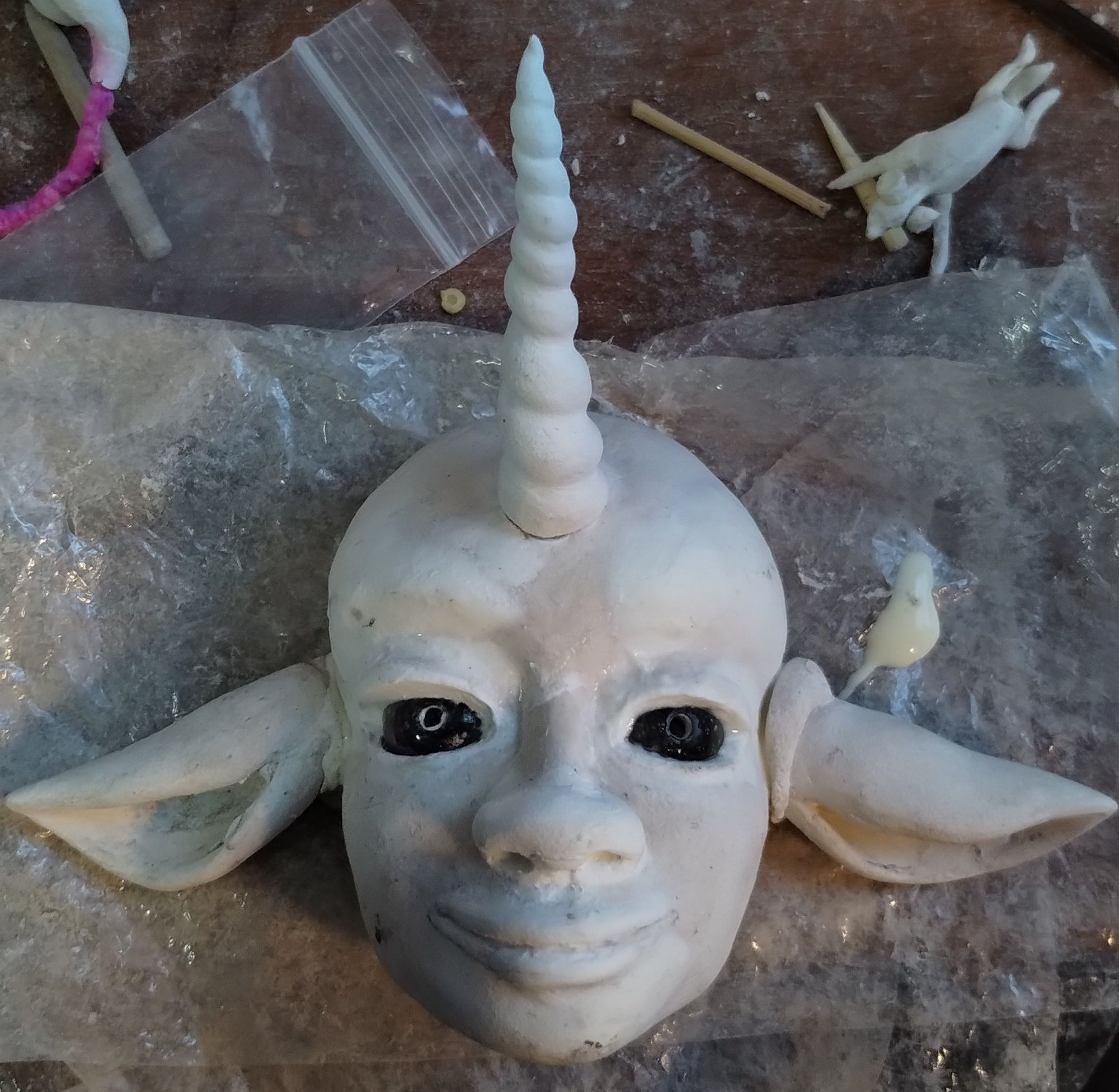 An unfinished humanoid doll with a unicorn horn and ears