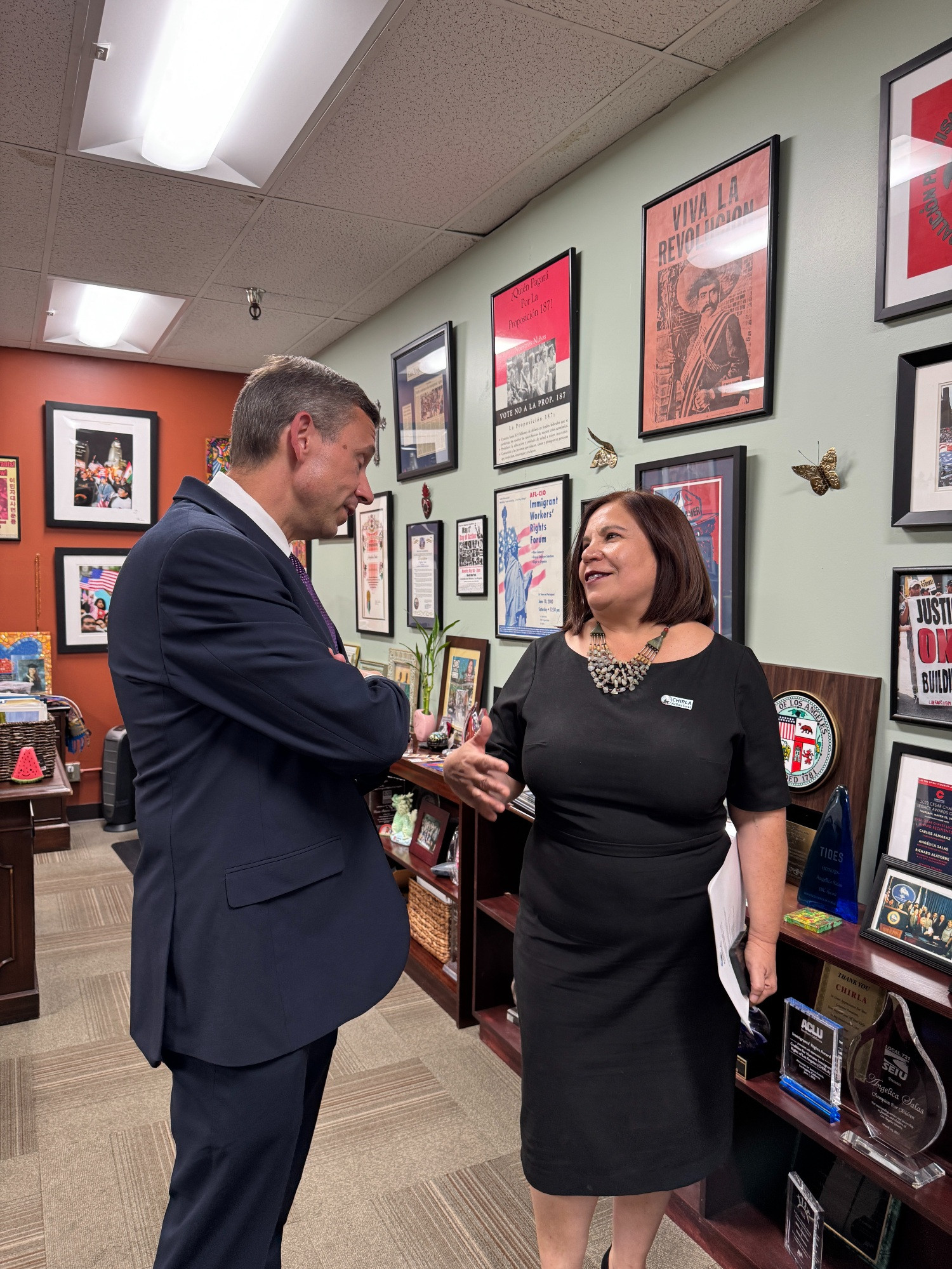 DNC Chair Ken Martin speaking with Angelica Salas, a national immigration activists and movement leader in her office. Behind her are framed posters on the wall.