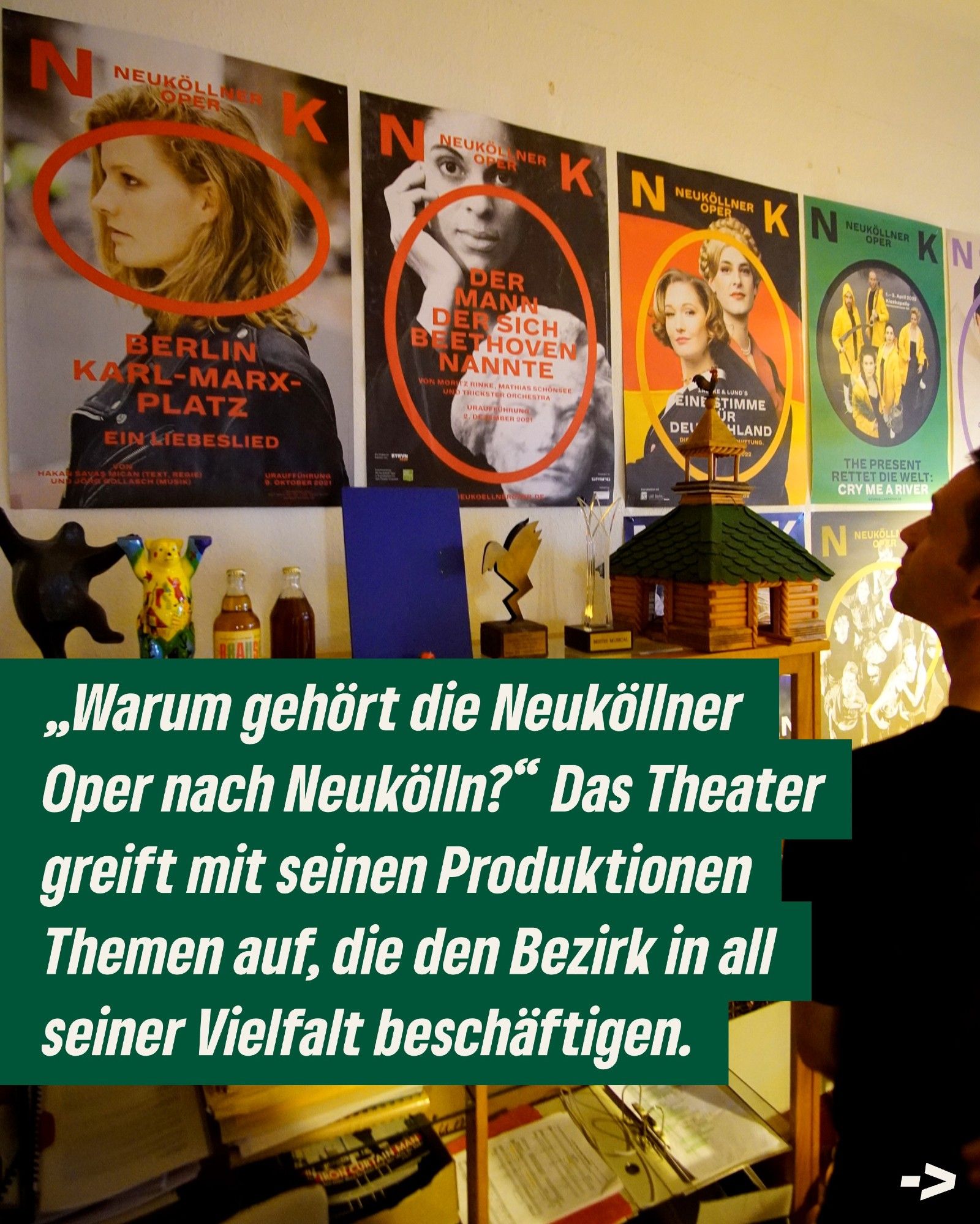 Das Bild zeigt eine Wand, an der Poster von Produktionen der Neuköllner Oper hängen. Unten links steht der Text: "Warum gehört die Neuköllner Oper nach Neukölln? Das Theater greift mit seinen Produktionen Themen auf, die den Bezirk in all seiner Vielfalt beschäftigen."