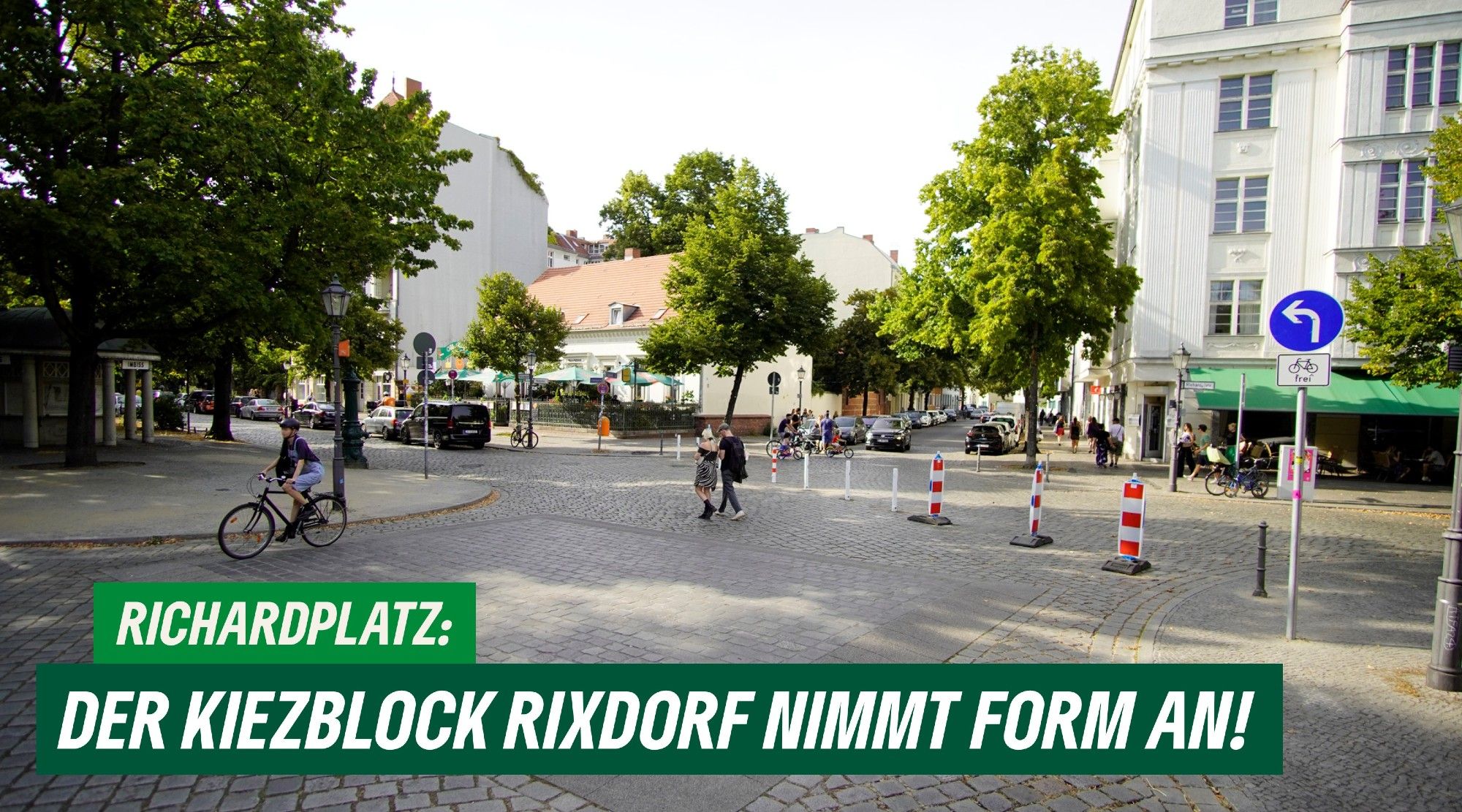 Das Bild zeigt den Richardplatz in Neukölln. Über die Kreuzung an der Ecke Richardstraße ist eine Diagonalsperre errichetet. Autos aus dem Süden müssen links abbiegen. Rechts steht ein Schild, dass dies anzeigt, darunter das Schild "Fahrrad frei". Im Bild sind mehrere spazierende oder fahrradfahrende Personen zu sehen. Unten steht der Text: "Richardplatz: Der Kiezblock Rixdorf nimmt form an!"