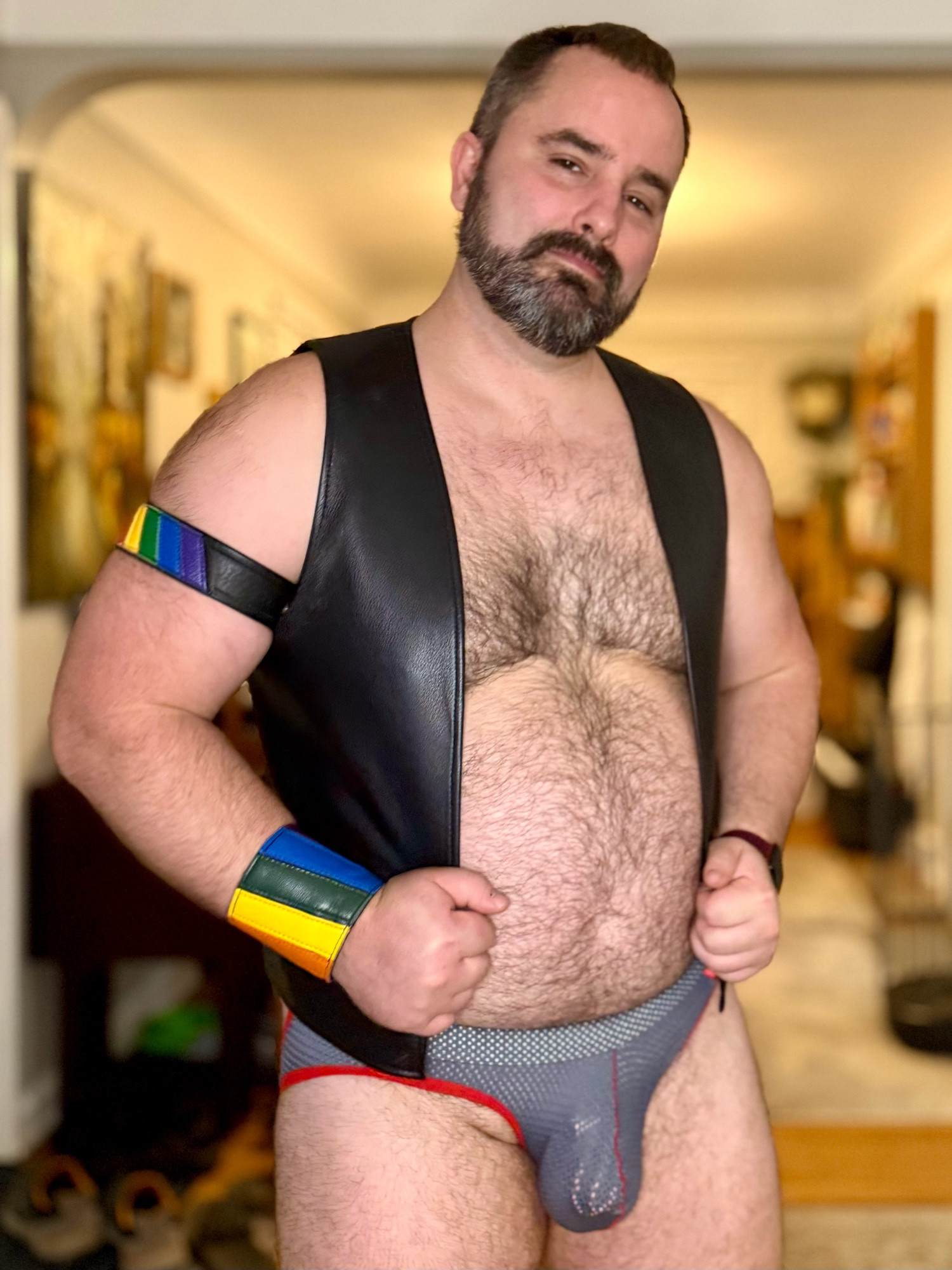 Photo of me in a mesh jockstrap and a black leather vest.  I have a leather armband and wristband on my right arm.  My pink cock cage is visible through my undies!