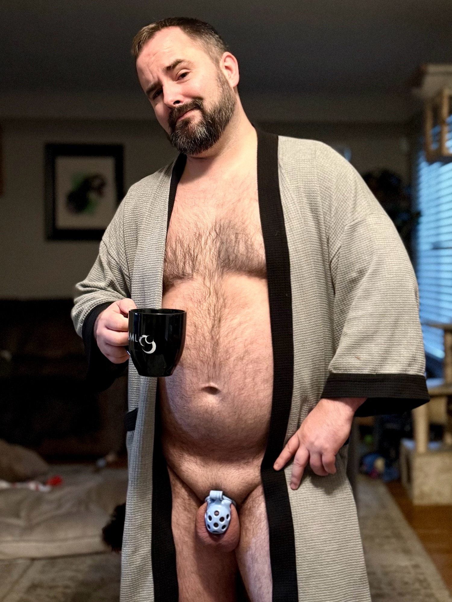 Myself standing in an open grey robe.  I’m holding a cup of coffee in one hand.

My round hairy belly is accentuated and my nub is locked away in a blue chastity cage.