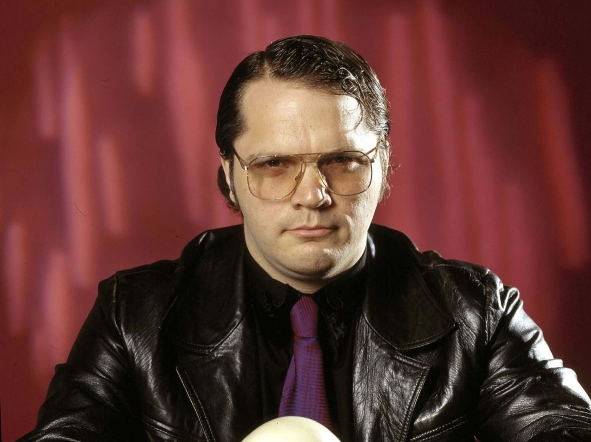 Garth Marenghi, a white man with dark slick hair and glasses, wearing a leather jacket, black shirt, and purple tie