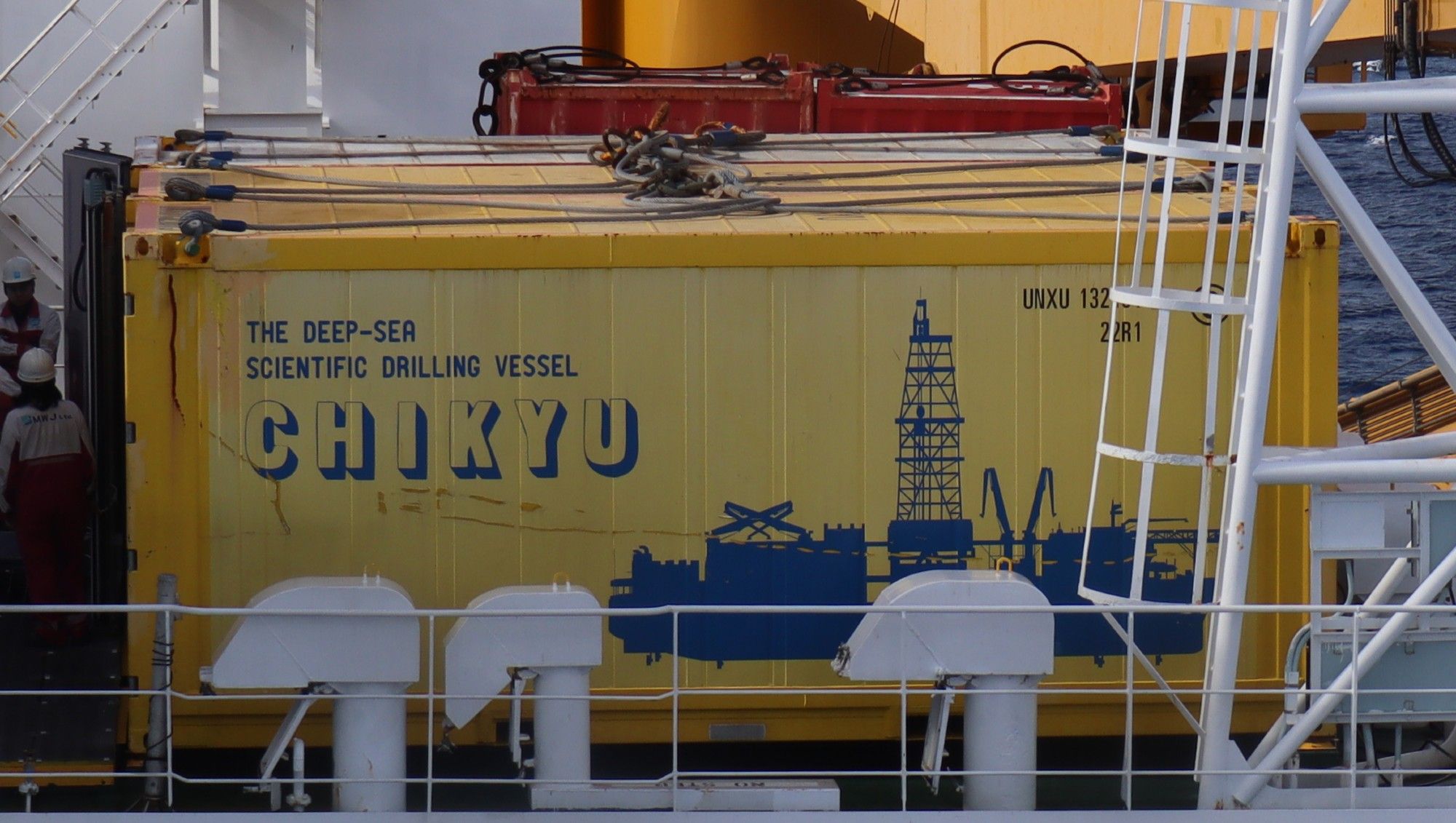 On the deck of the drilling vessel Chikyu is a yellow/orange shipping container decorated with a blue silhouette of the ship, and the words "The Deep-Sea Scientific Drilling Vessel CHIKYU" --- It looks cool!