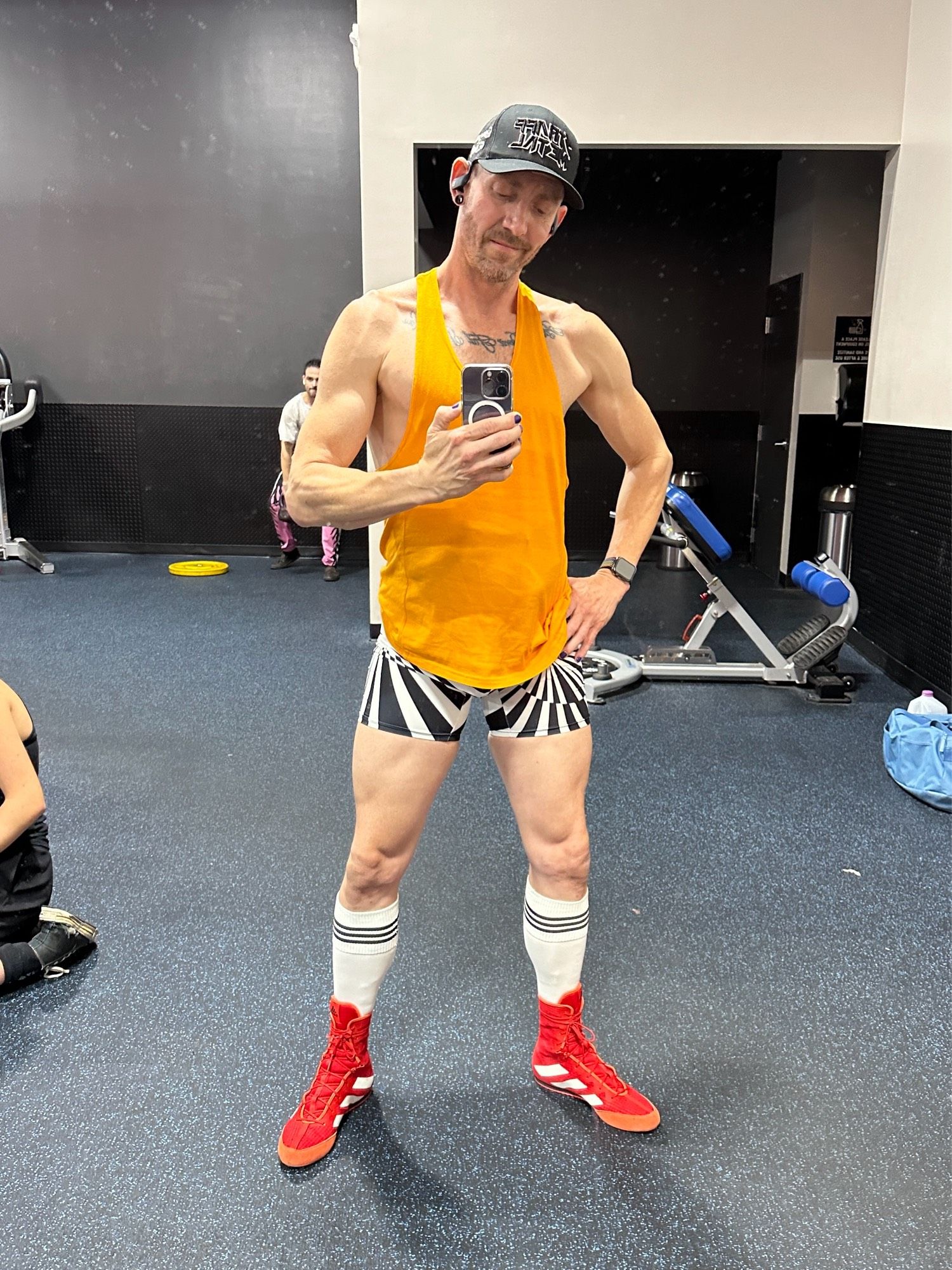 Gym selfie of me. Wearing black and white graphic hot shorts and an orange stringer tank.