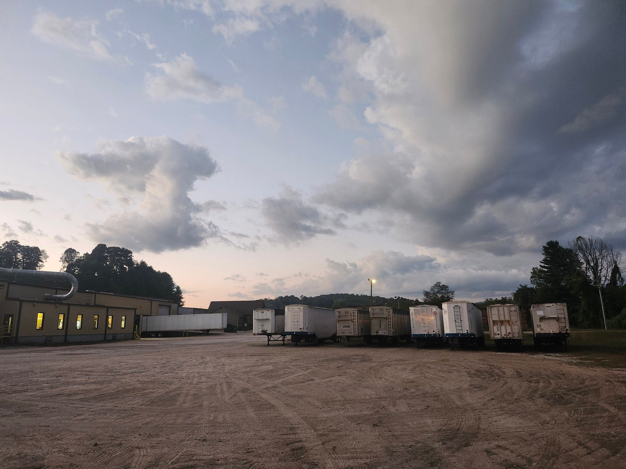 Picture of a trailer parking lot, the sky is overcast with the sun setting behind a building.