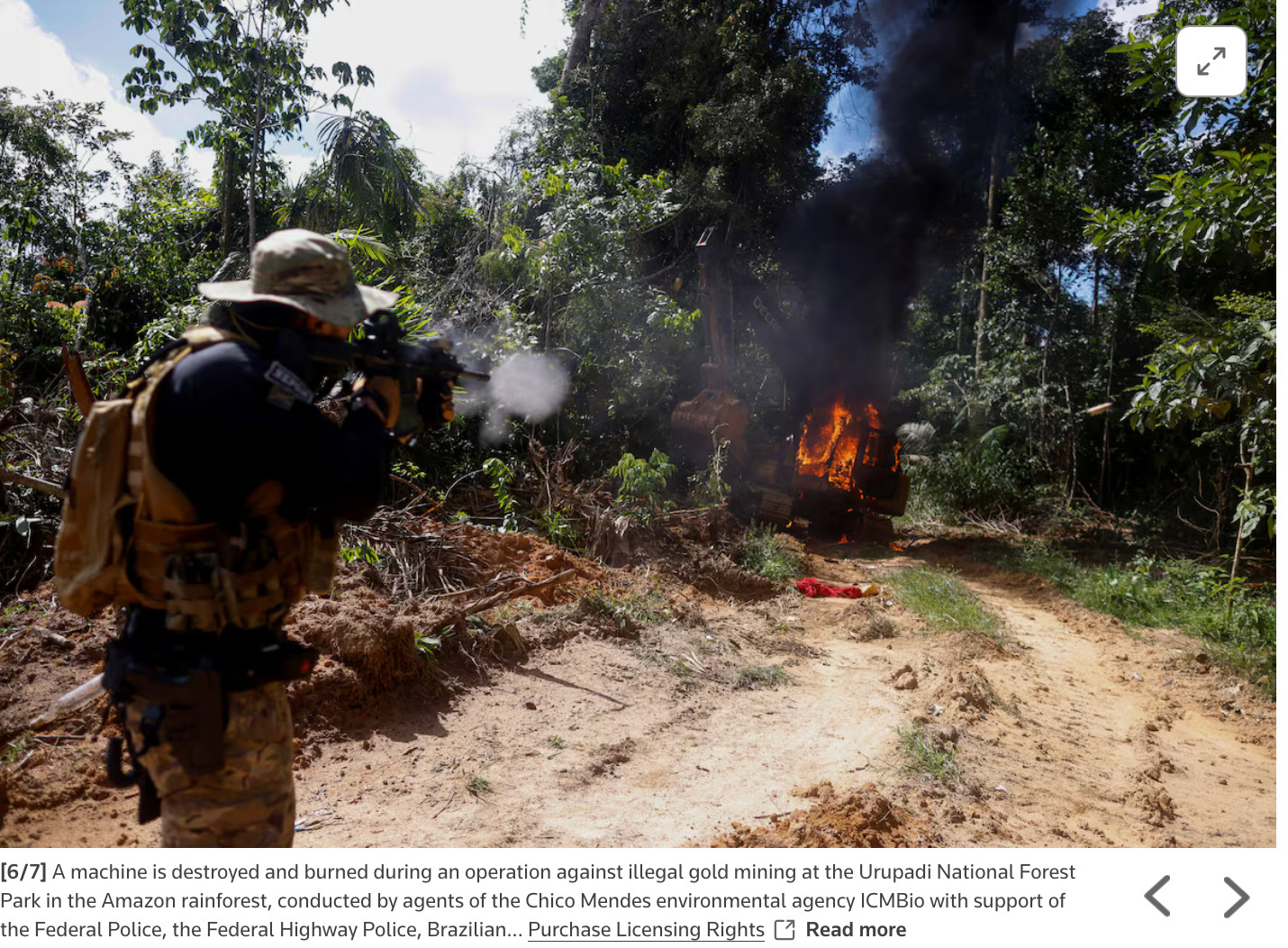 A man fires a weapon in the forest at a burning excavator