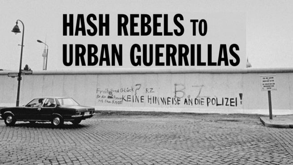 Das Bild zeigt eine Straßenszene in Schwarz-Weiß mit einem geparkten Auto vor der Berliner Mauer. Auf der Mauer steht in großen Buchstaben: „Hash Rebels to Urban Guerrillas“. Darunter ist Graffiti zu sehen: „Keine Hinweise an die Polizei!“ Ein Schild ist rechts im Bild sichtbar.