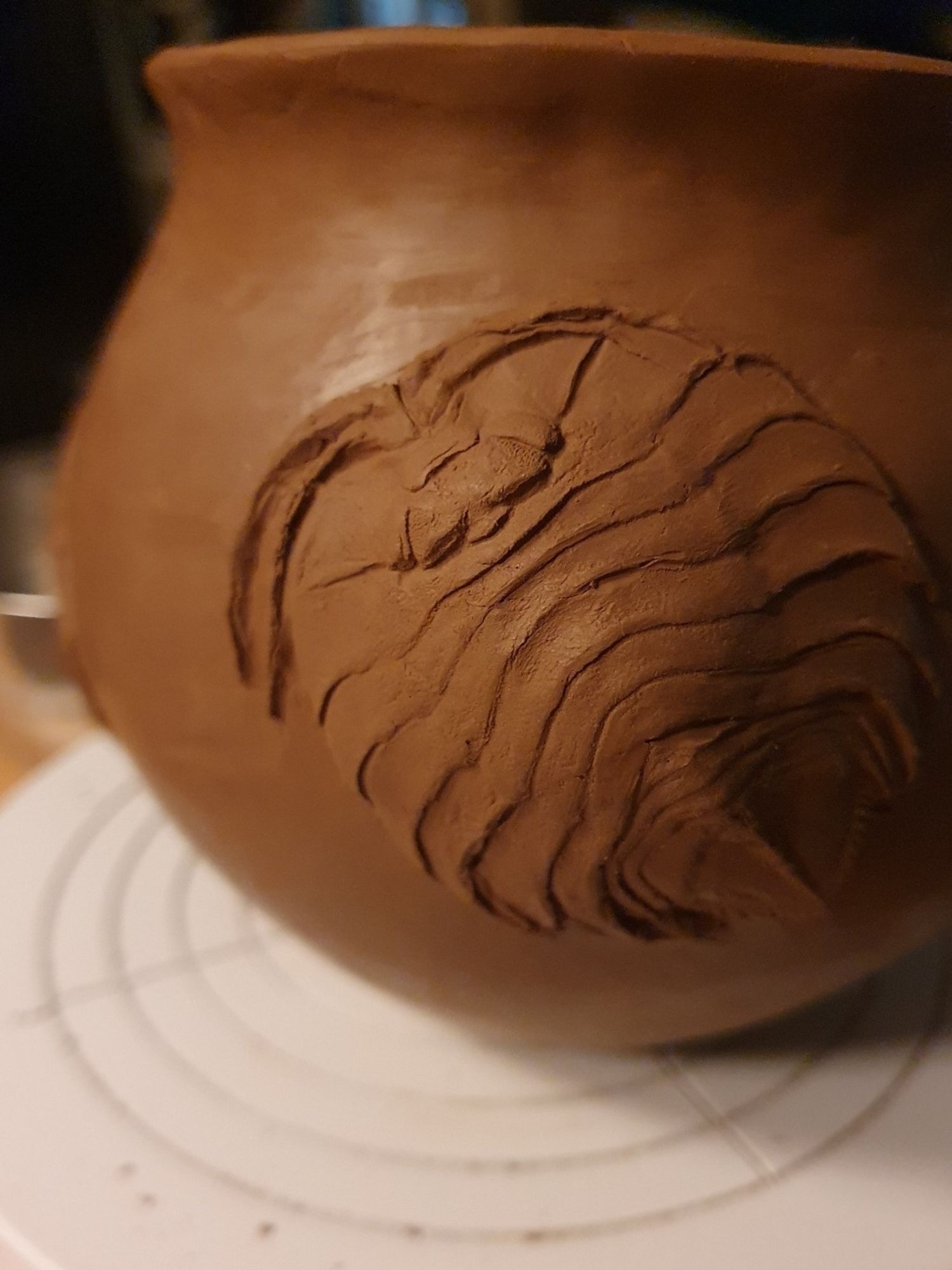 Detail of a hand sized ceramic jar with a Ceratoserolis isopod decor in relief. Clay is red-brown, still being worked on a white rotating tray