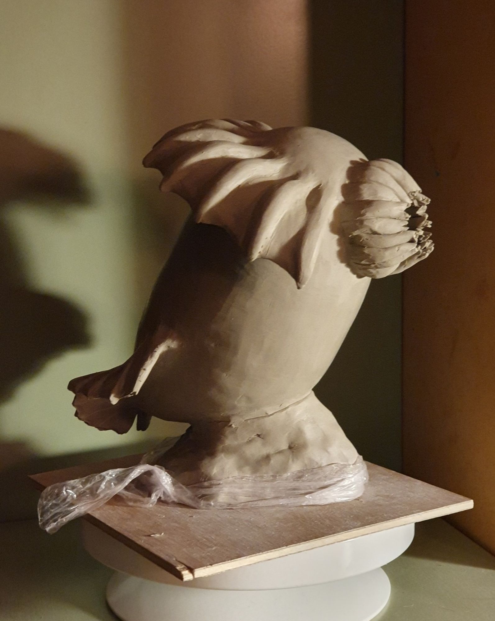 Clay sculpture of a headless chicken monster in profile with dramatic lighting on a small plank.