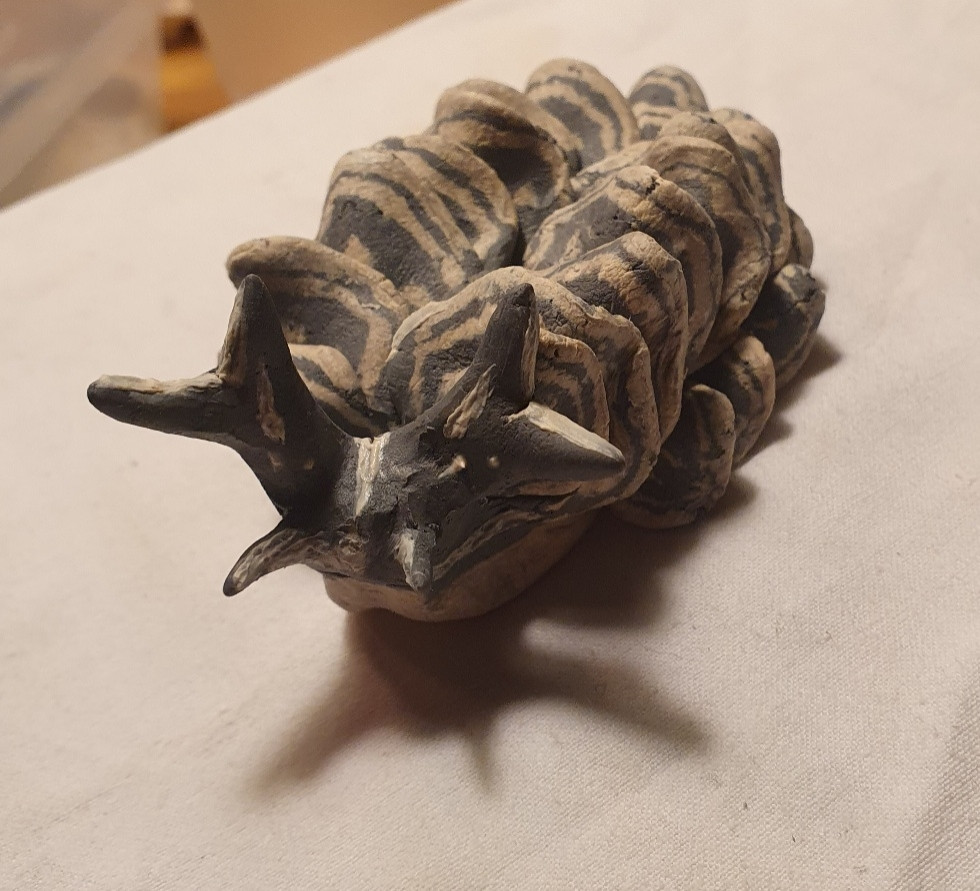 Rough ceramic black and white sacoglossan with patterned scales from front . Slip painted head with tentacles.