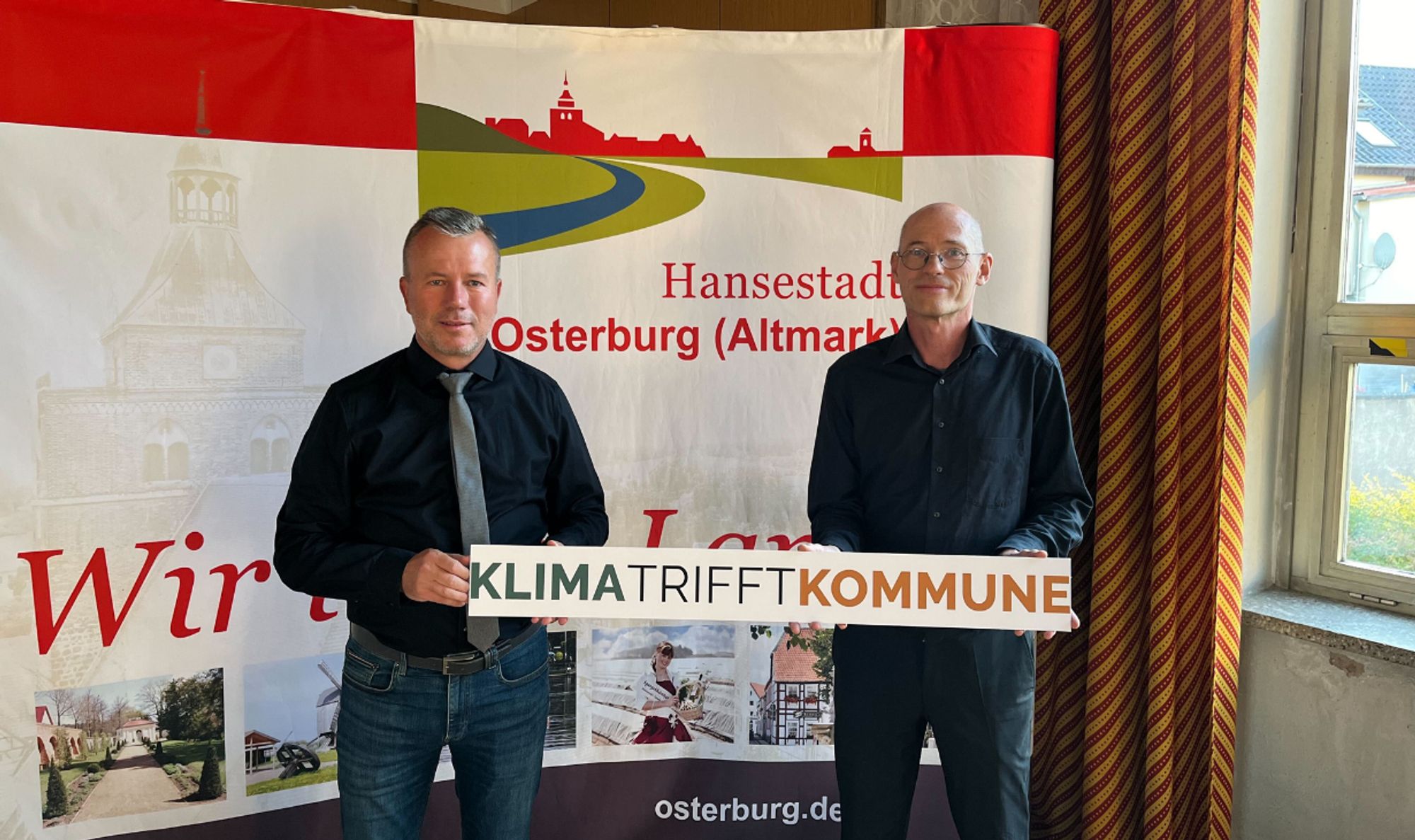 Bürgermeister Nico Schulz mit Projektleiter Michael Efler. Sie halten ein Schild mit der Aufschrift: "Klima trifft Kommune".