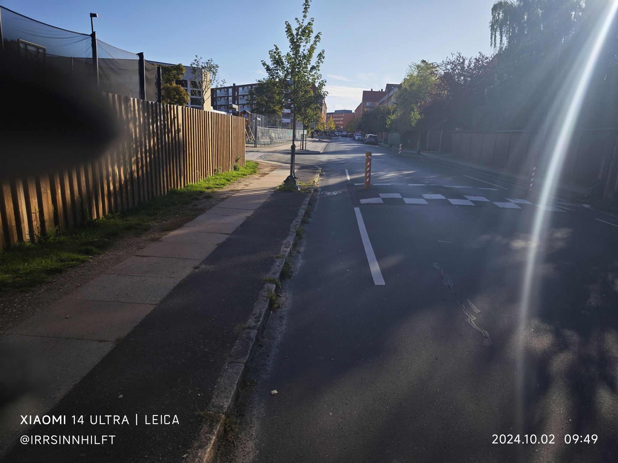 Eine Straße. Mittig eine Fahrspur die über ein weiß markiertes und mit zwei Pollern begrenztes Hindernis führt.
Rechts und Links davon der Bypass für Radfahrende mit Radsymbol