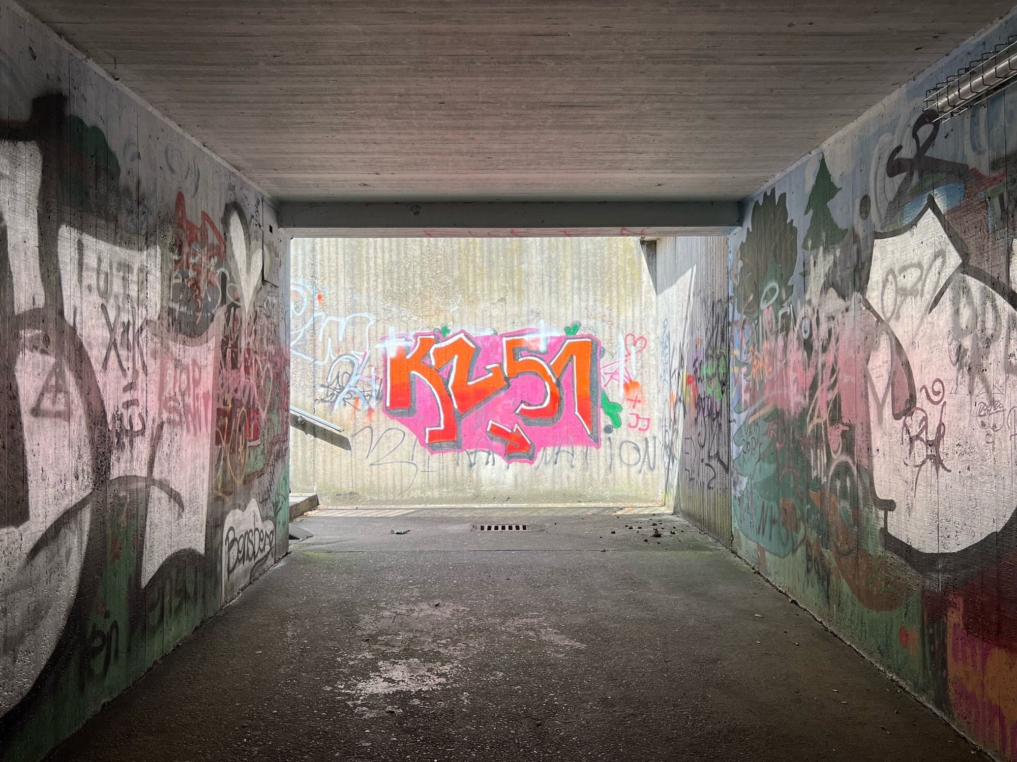 A graffitto reading KZ51 in bright orange on pink at the end of a concrete tunnel