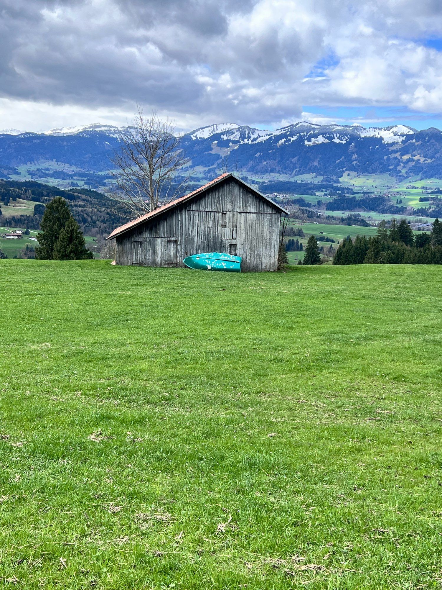 A turquoise boat leaning against a wooden shed on an alp high up in the mountains. Snow covered peaks in the background.