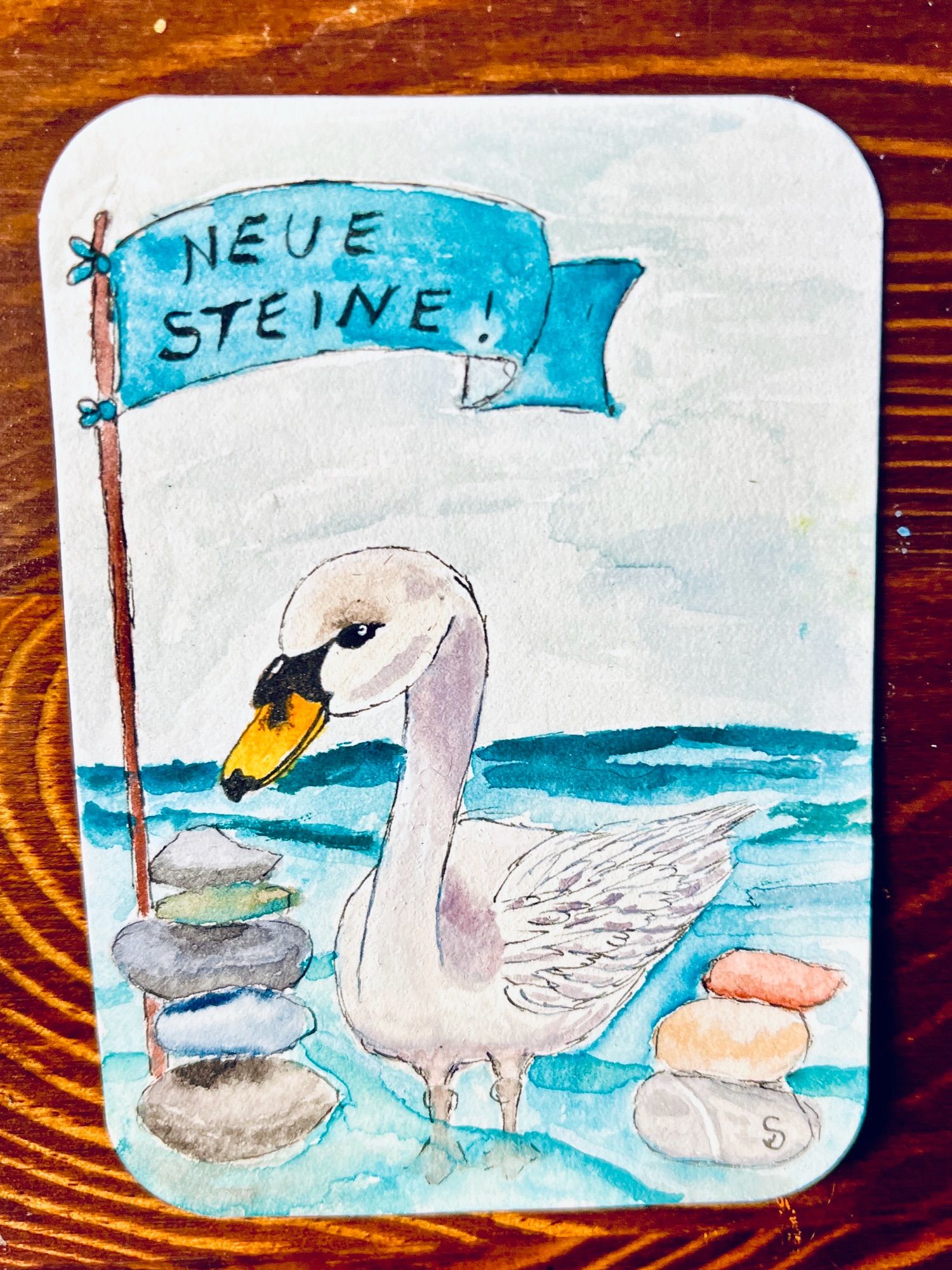 Schwan steht im niedrigen Wasser. Zu beiden Seiten ein Stapel Steine. 
Darüber eine Flagge, auf welcher „Neue Steine!“ steht.