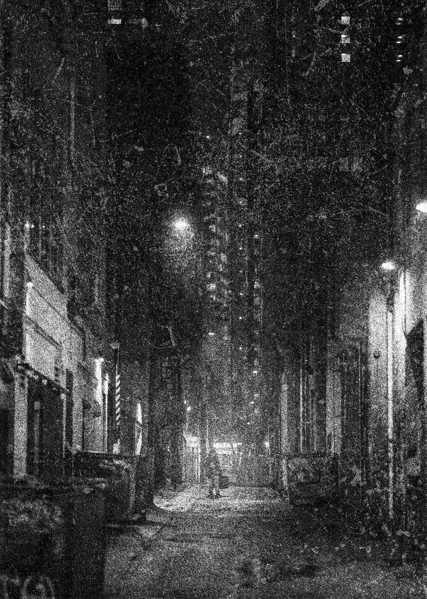 Heavily stylised black and white image of a desolate alley with a single figure at the centre, carrying a heavy suitcase.