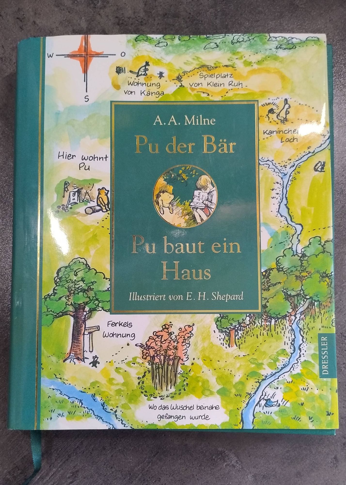 A.A. Milne, "Pu baut ein Haus." Das Kinderbuch liegt auf einer dunkel marmorierten Oberfläche.