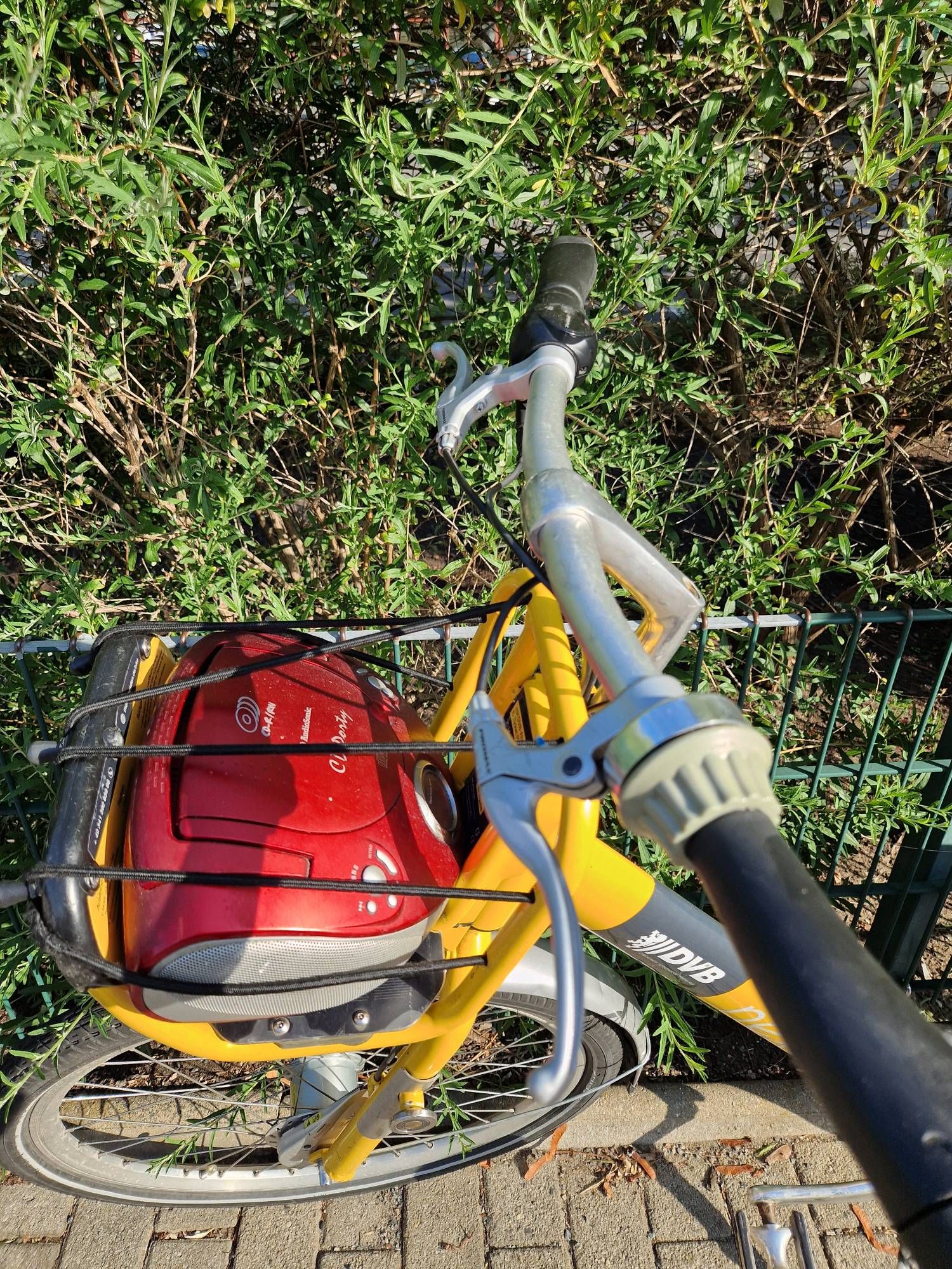 Ein Mobibike-Fahrrad der Stadtverkehrsbetriebe Dresden steht vor einem Zaun. Auf den vorderen Gepäckträger hat Jemand einen CD-Rekorder gespannt, so dass Jeder, der es ausleiht, während der Fahrt Musik hören kann.