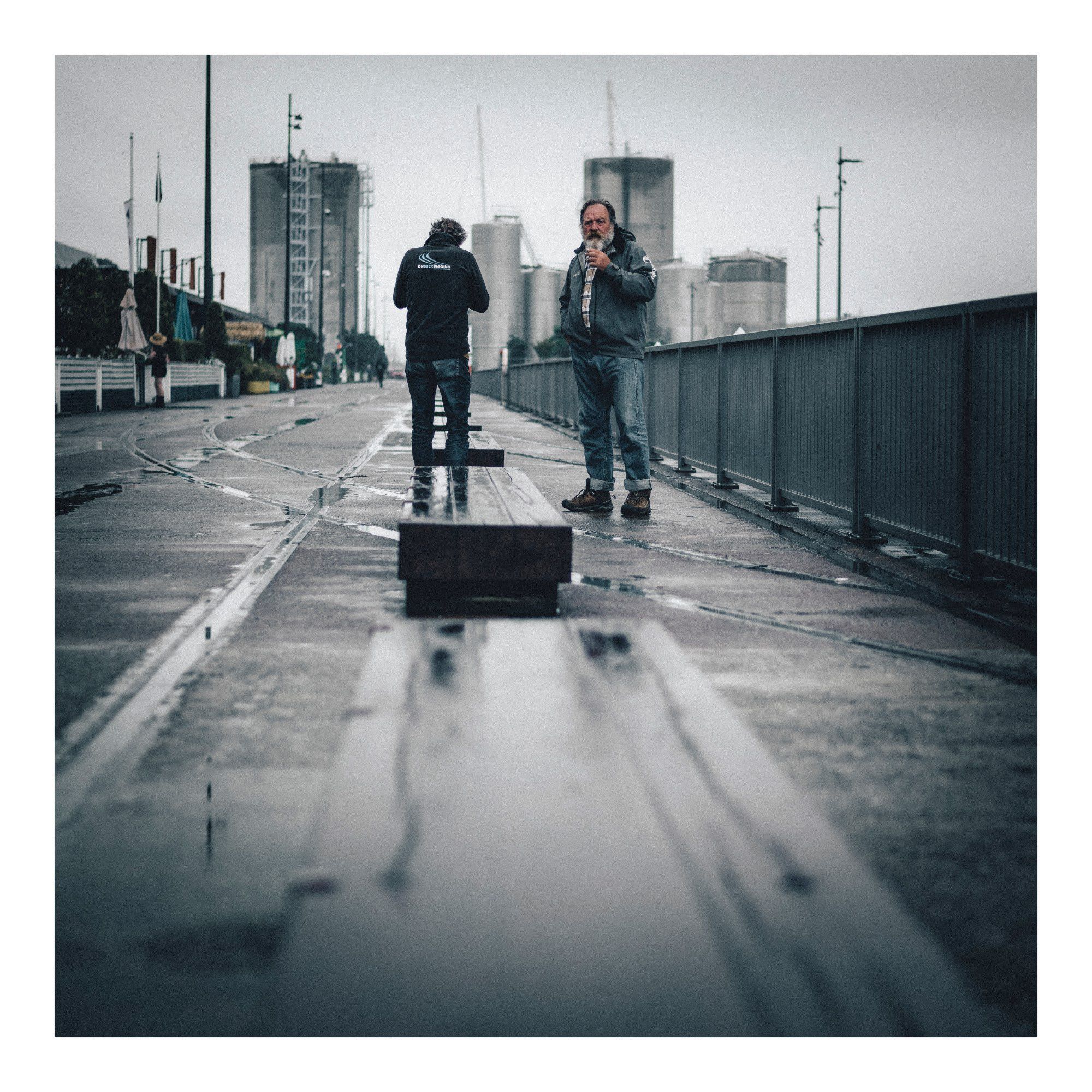 couple of dudes having a smoke on the waterfront down at the Viaduct in Auckland, not happy I'm shooting them.  Low angle photo = industrial look, overcast & wet day so quite grim looking photo