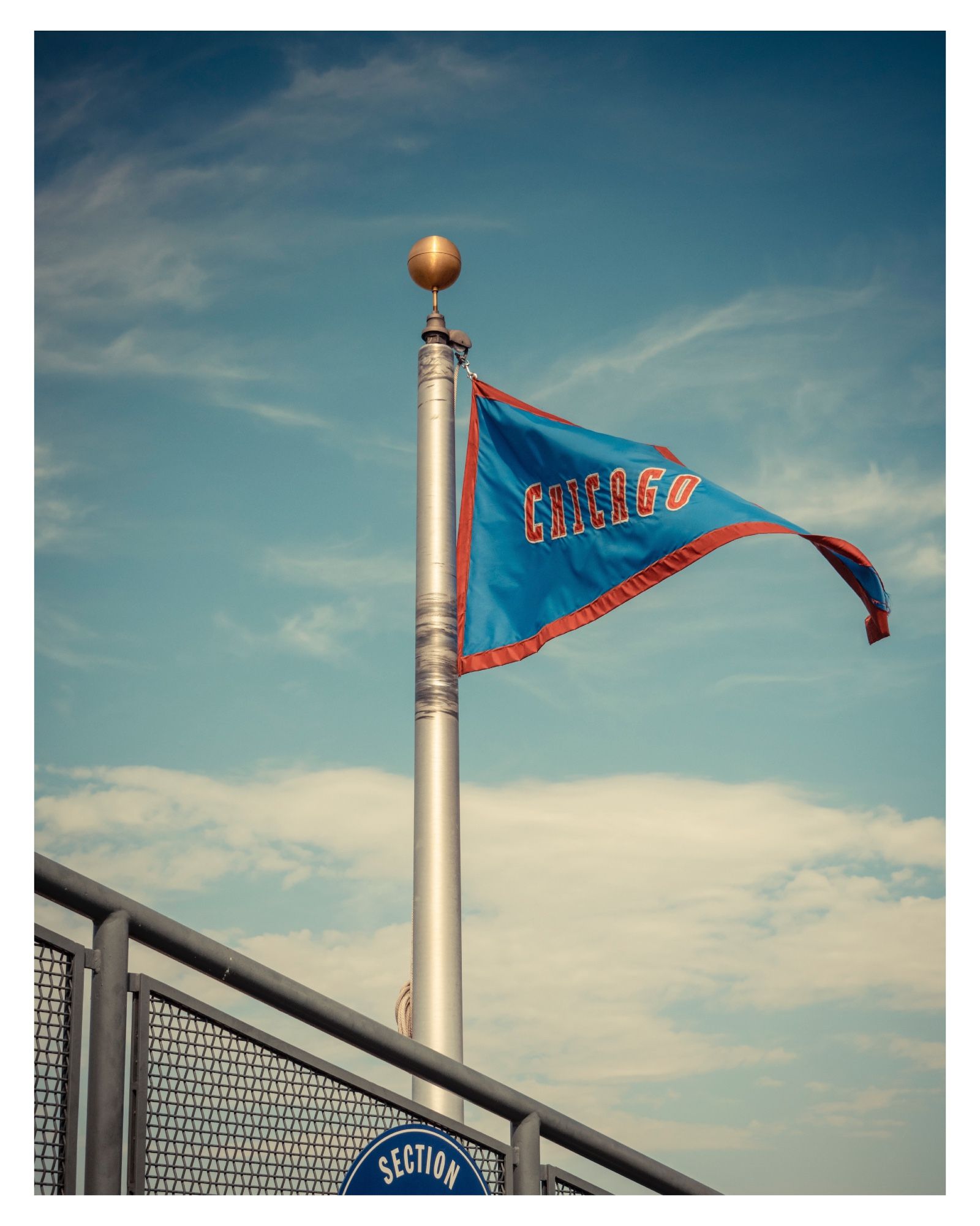 Chicago Cubs Flag flying above Coors Field, the home of the Colorado Rockies MLB baseball team.  Smoky blues & muted pale yellows, but trying to emulate Kodak Ektachrome film look, the red trim on the blue flag really pops.