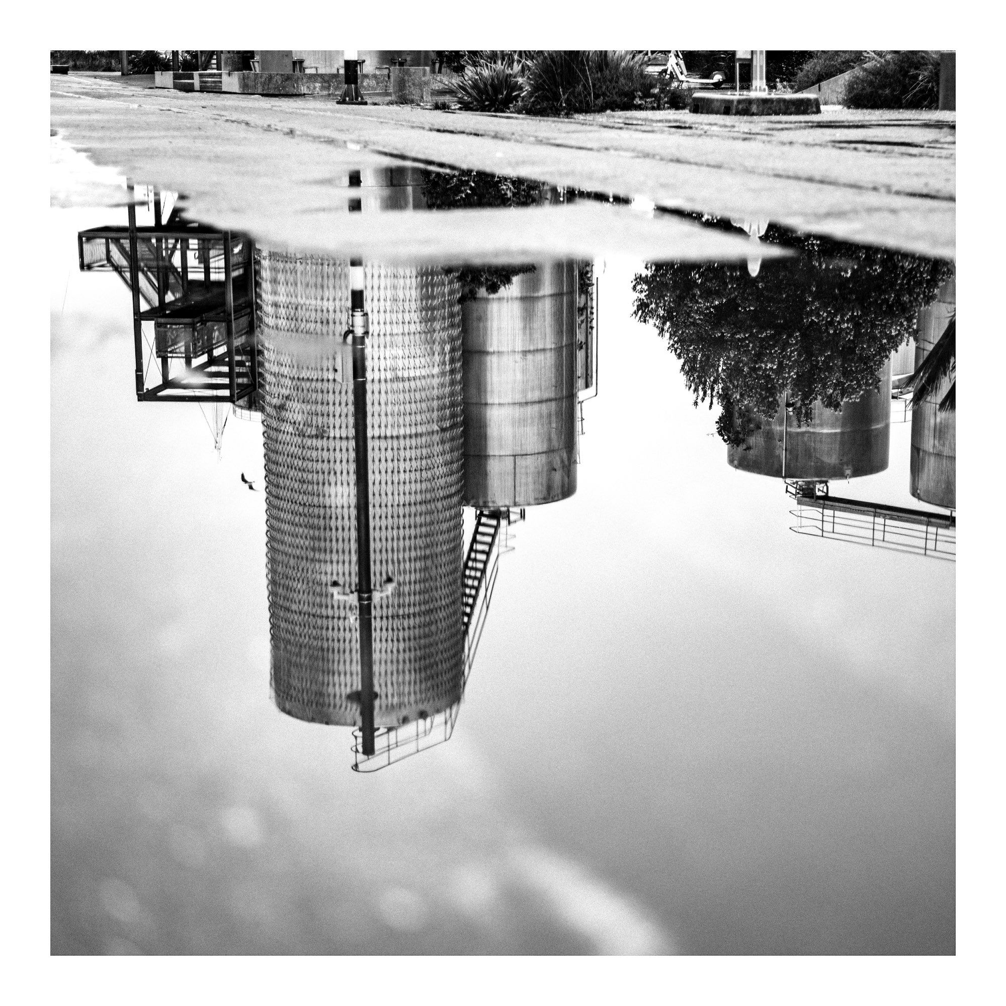 a photo of some old silo tanks on Auckland's waterfront reflected in a puddle. Black & white grim art