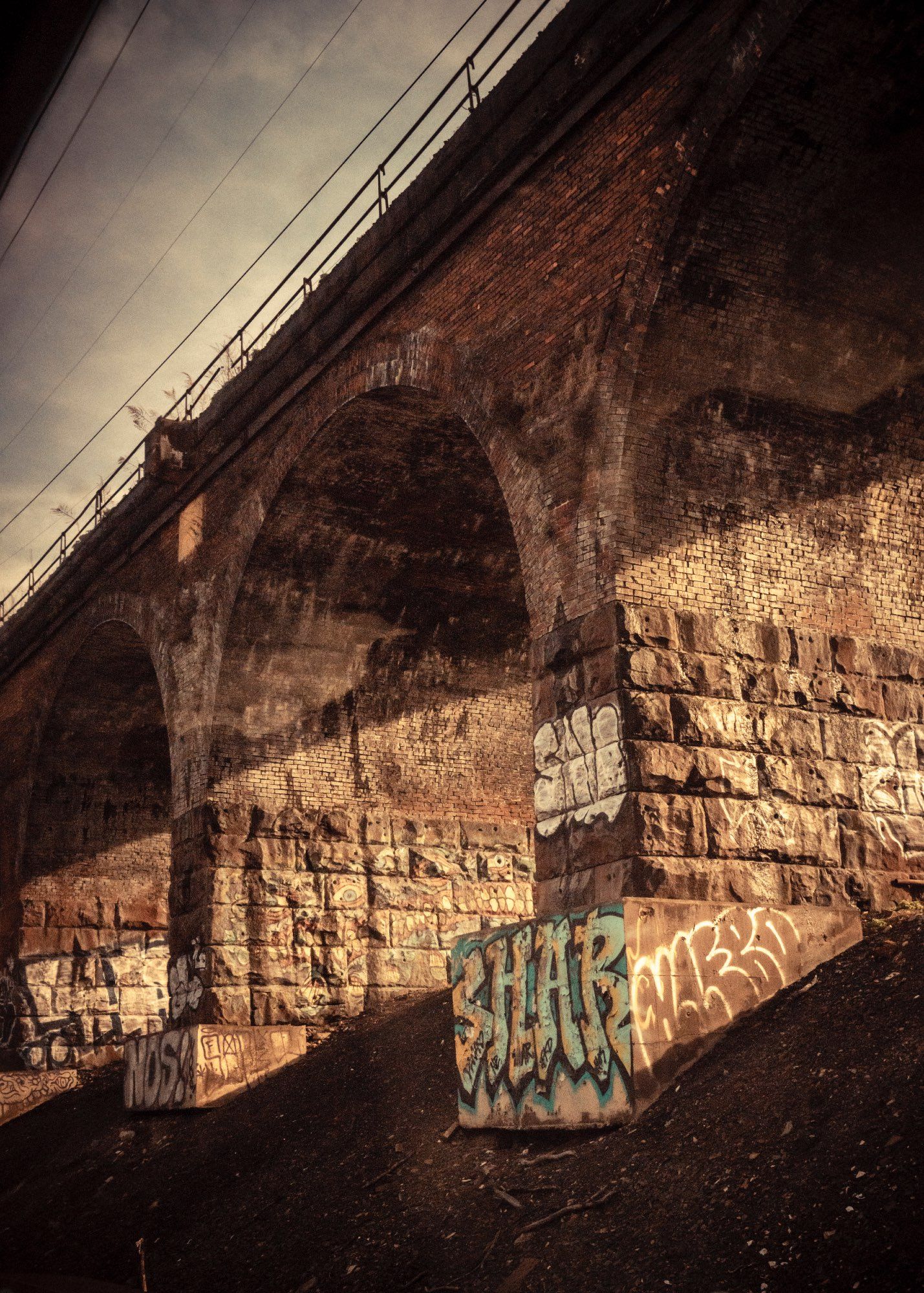 An old stone bridge as seen from below out of my train windows. Muted brown colours from warm evening early summer sun