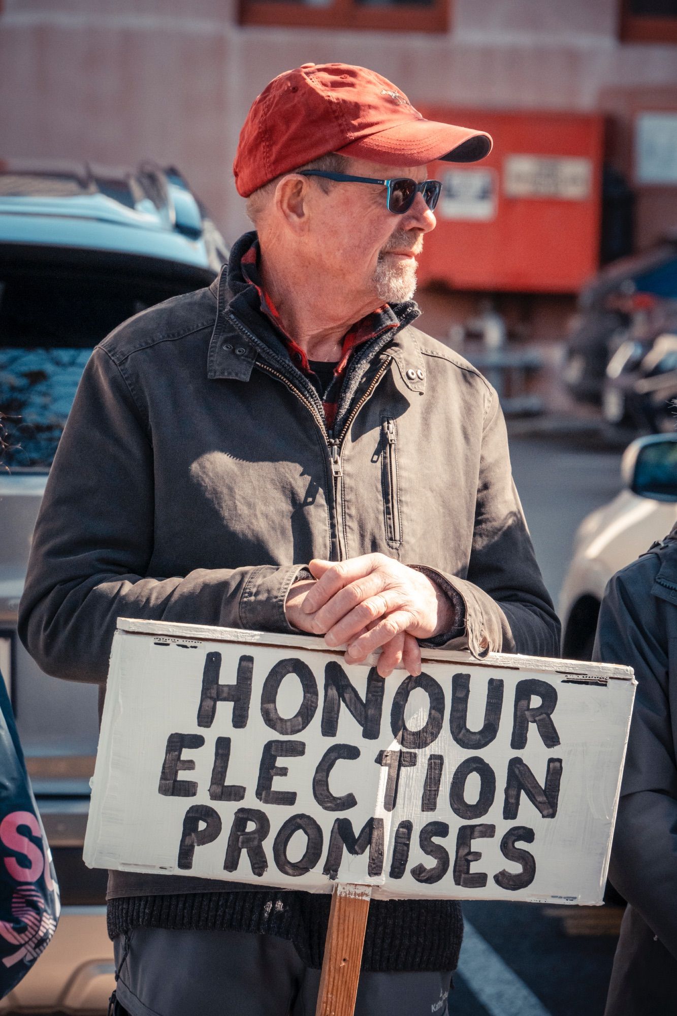 A man in a hat holding a sign saying 'Honour Election Promises'