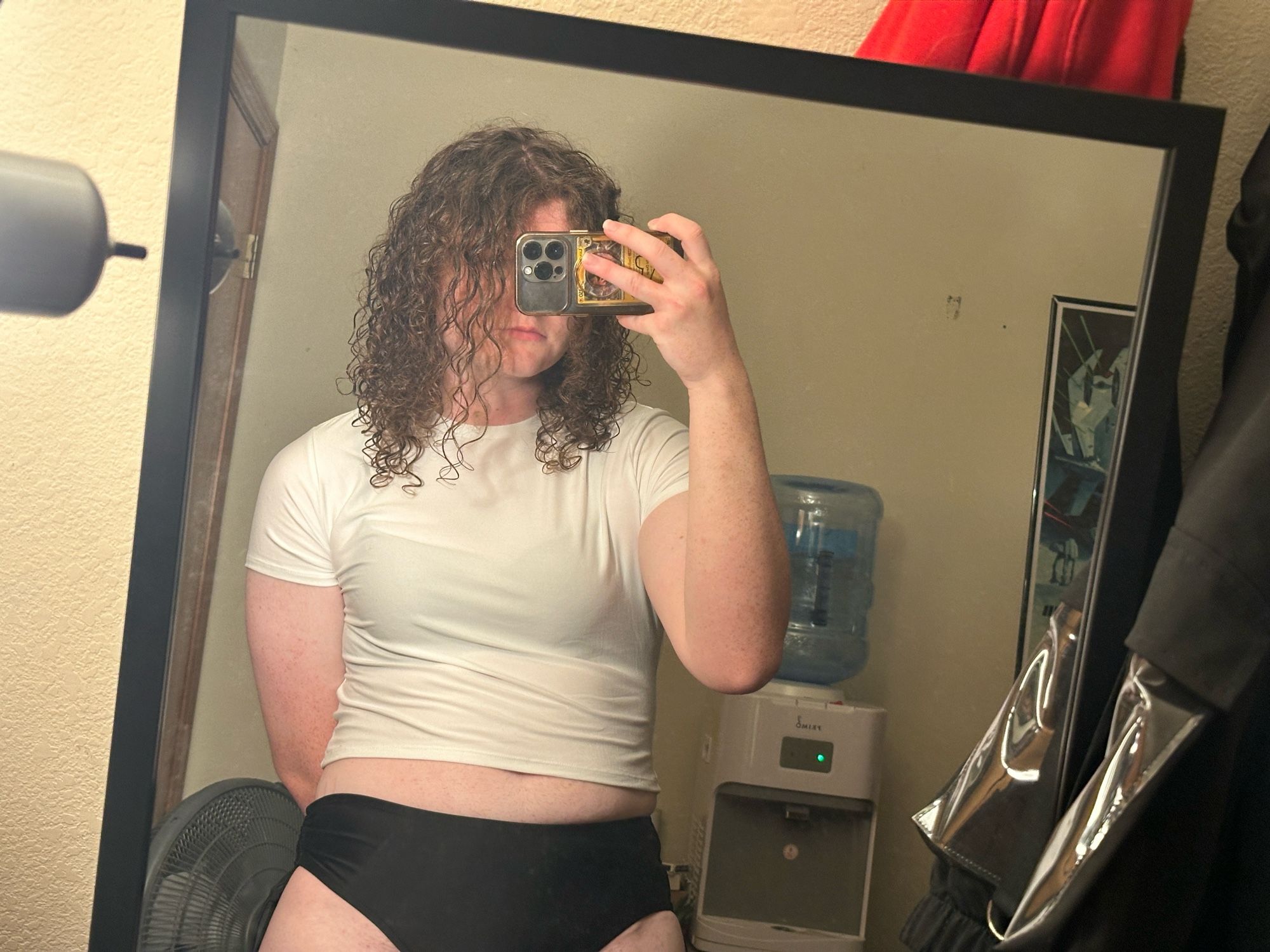 a mirror selfie of me wearing a semi transparent white tight shirt with my black bra peaking through and also wearing black panties and my arm is tucked behind my back