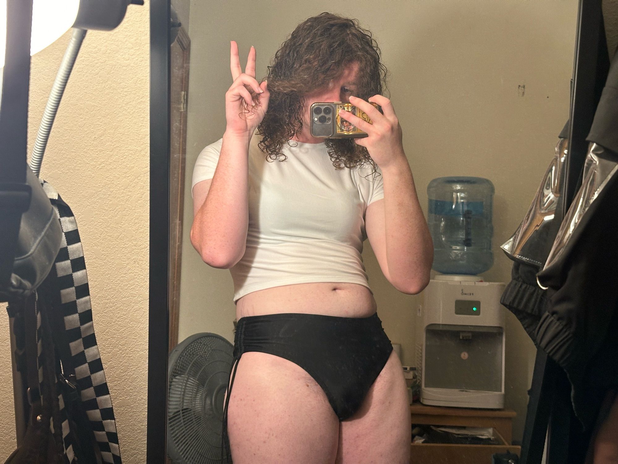 a mirror selfie of me wearing a semi transparent white tight shirt with my black bra peaking through and also wearing black panties and my ass bulge is pointed out and i’m making a peace sign