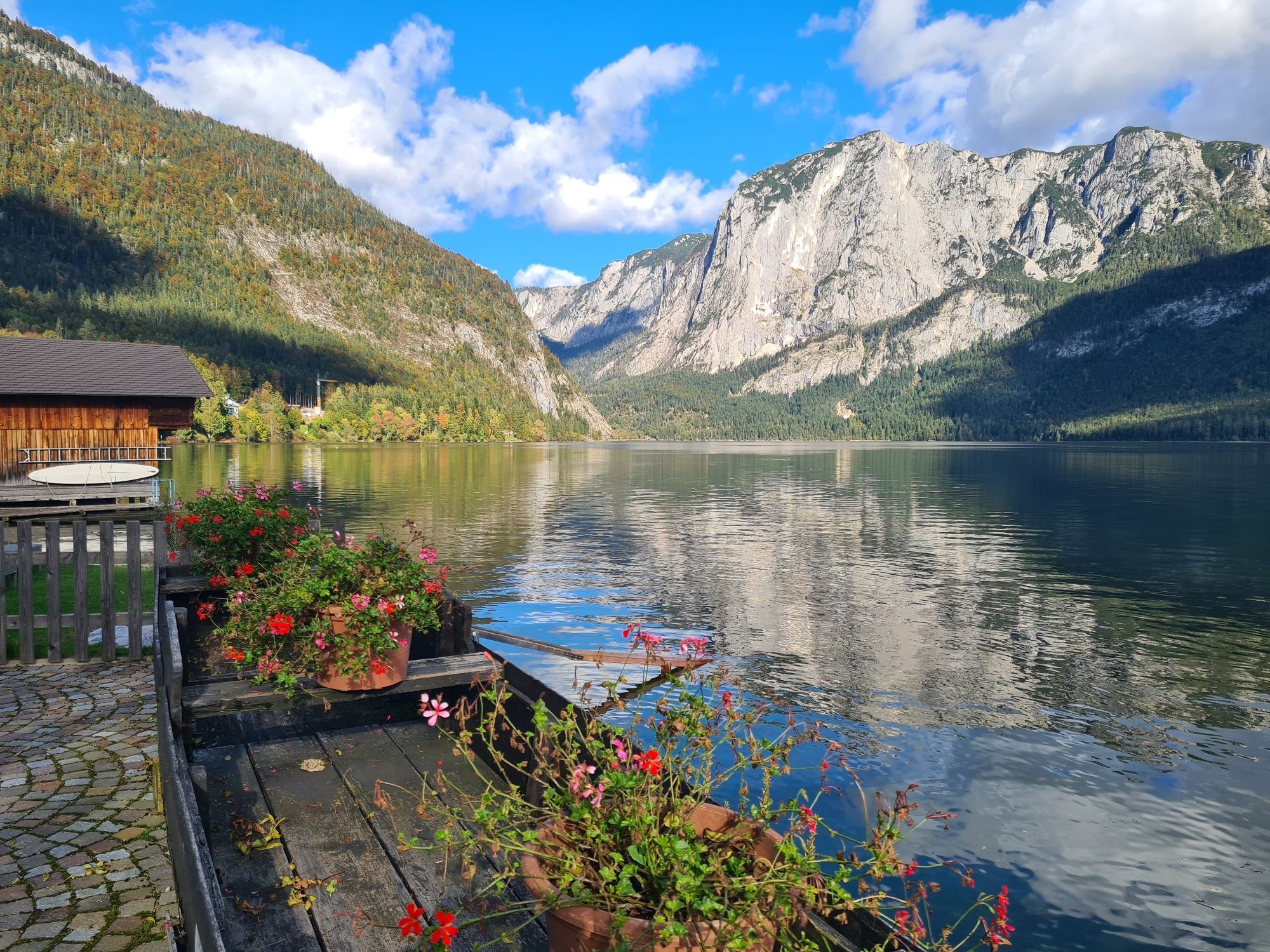 see mit Bergen im Hintergrund die sich OM wasser spiegeln und links Blumen am Steg