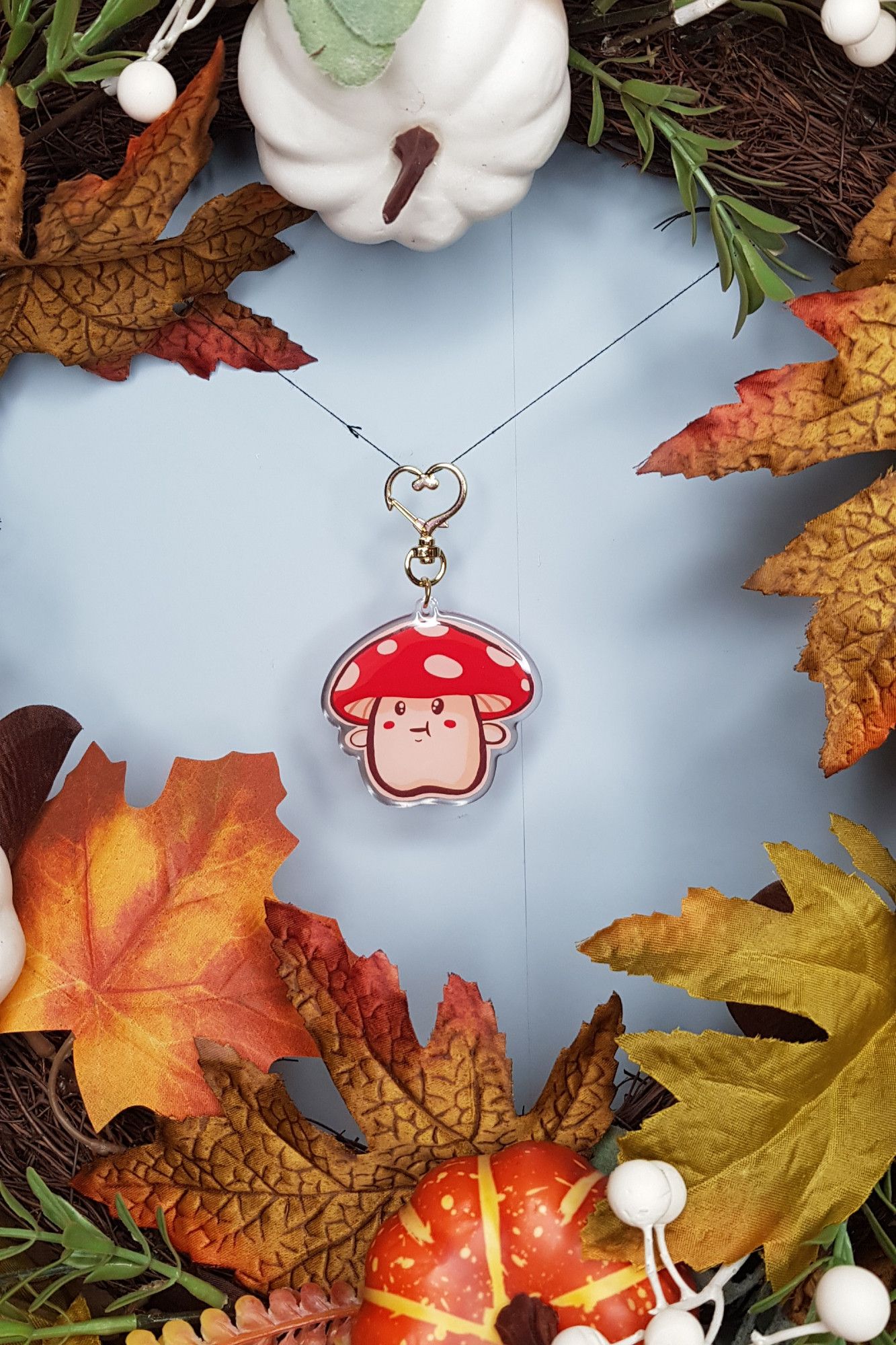 a photo of a red and white cap mushroom keychain that is hanging from a string in the middle of an autumn wreath.