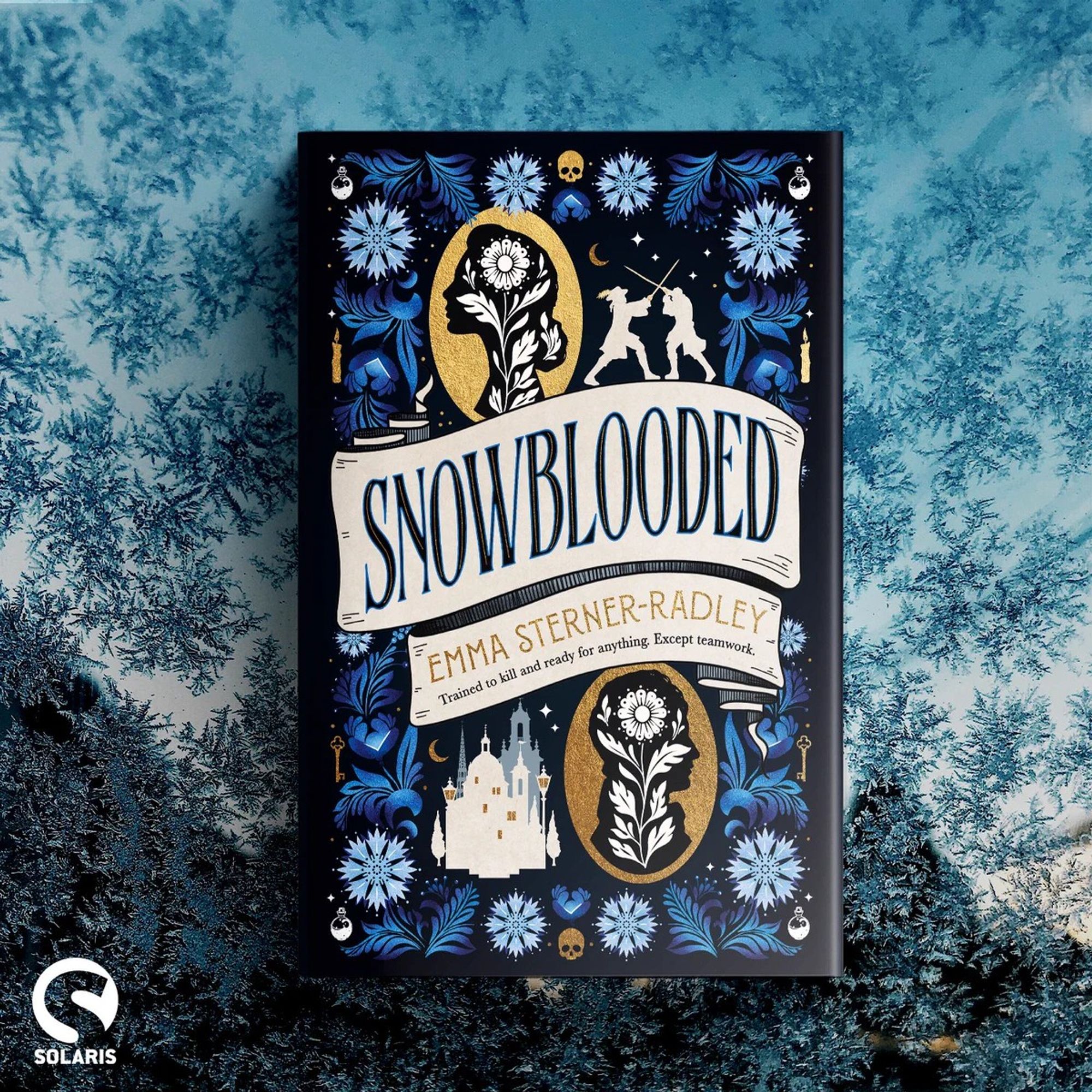 Image Description: against a background of snowflakes lies a hardback copy of SNOWBLOODED by Emma Sterner-Radley, the white Solaris logo is in the bottom left corner.