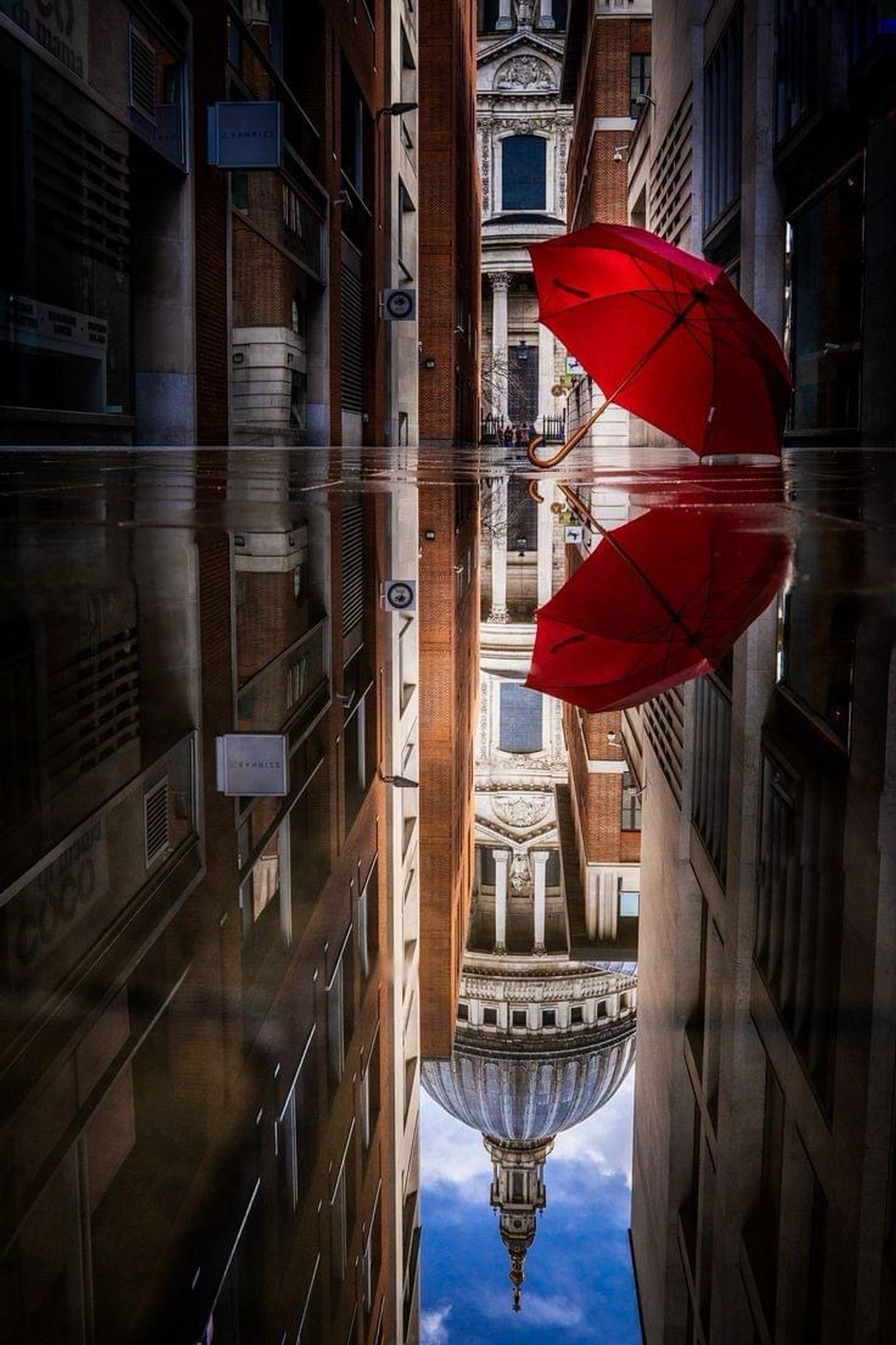 Reflet d’une rue dans sol trempé par la pluie 
Parapluie rouge posé par terre