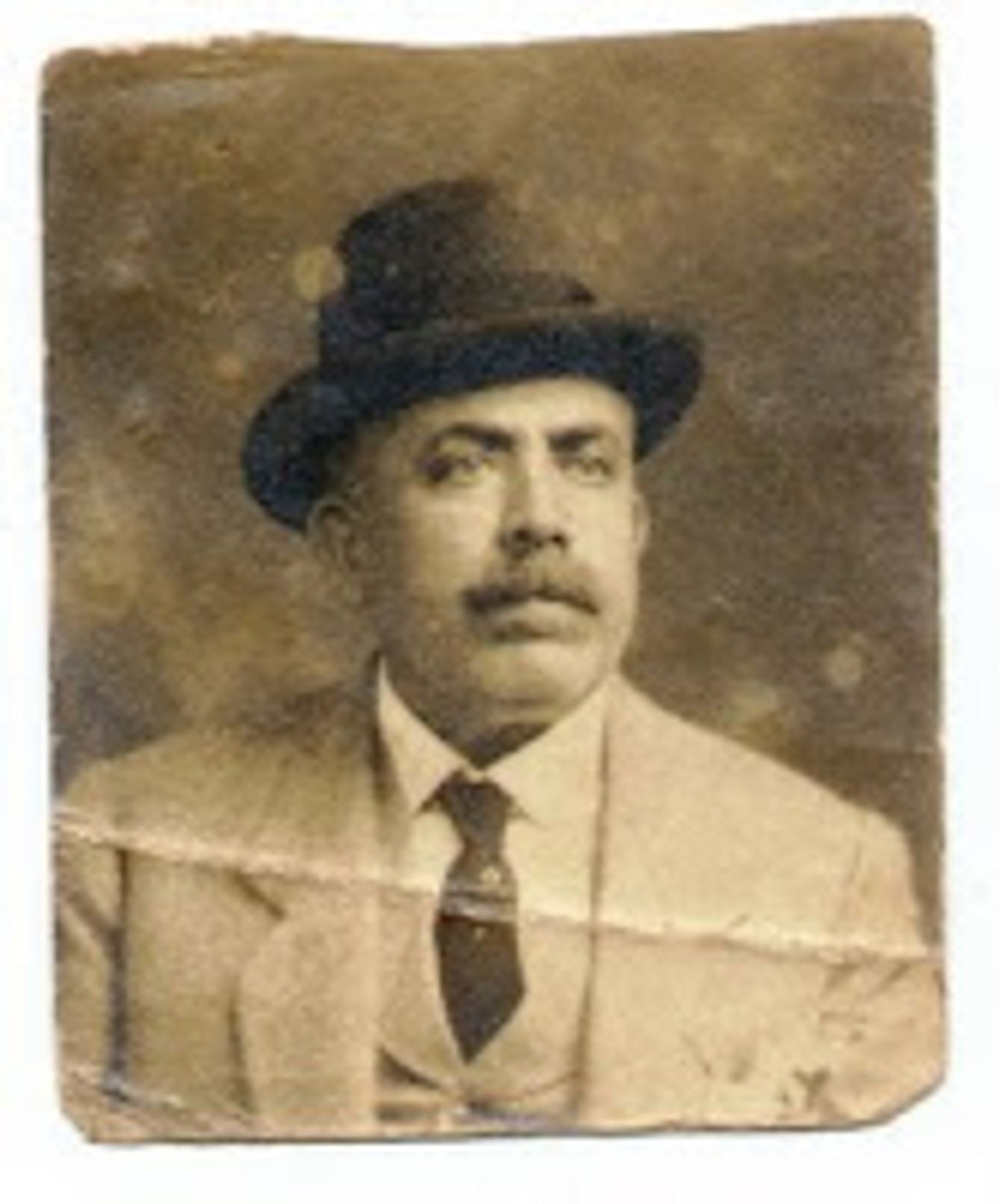 foto antiga [meio preto e branco meio sépia] de homem branco de chapéu e terno completo com paletó colete gravata e camisa. bigode