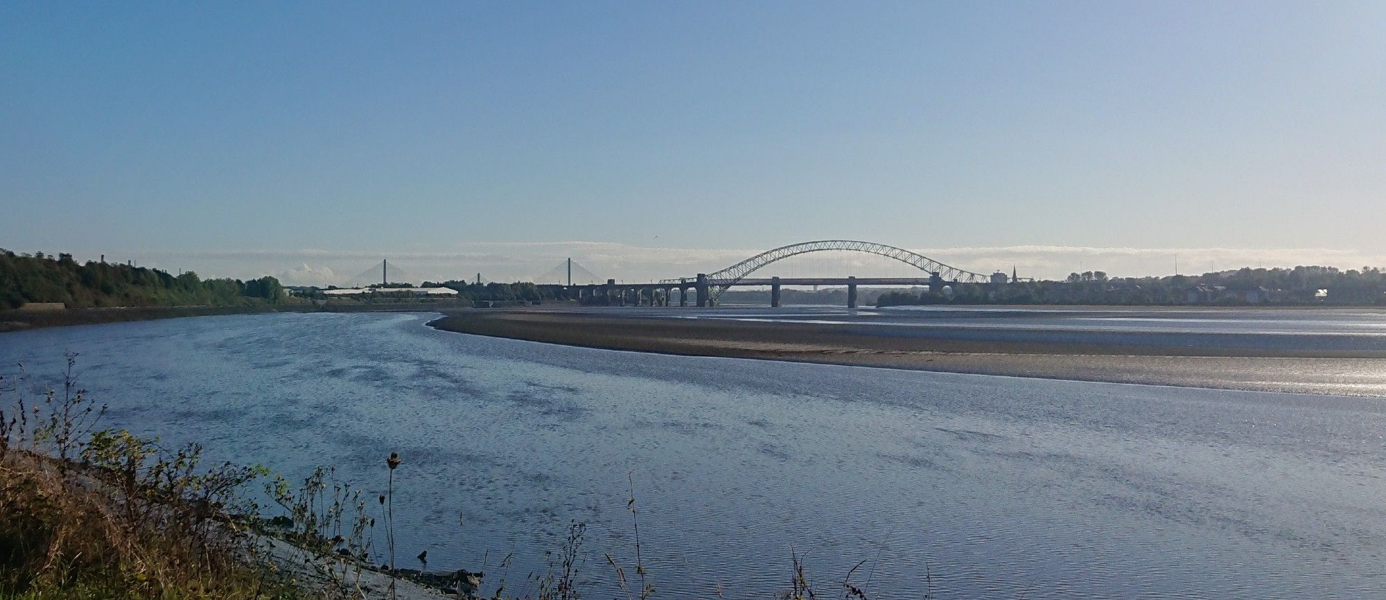 The industrial Mersey Estuary with both Runcorn bridges in the background. Blue water and sky on a lovely morning.