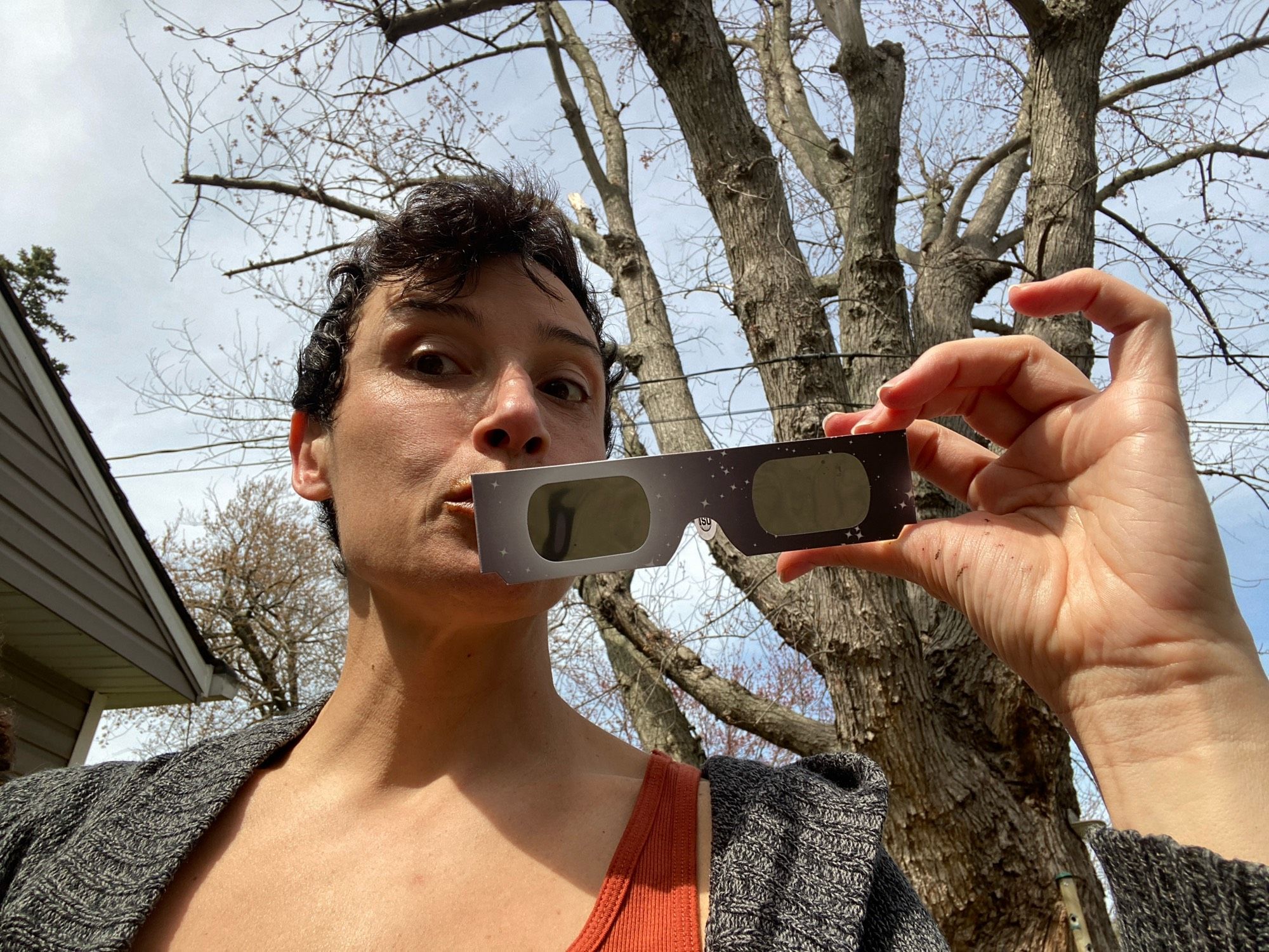 Brandy holding solar glasses with a dimming sky behind (neck and face from down-up)