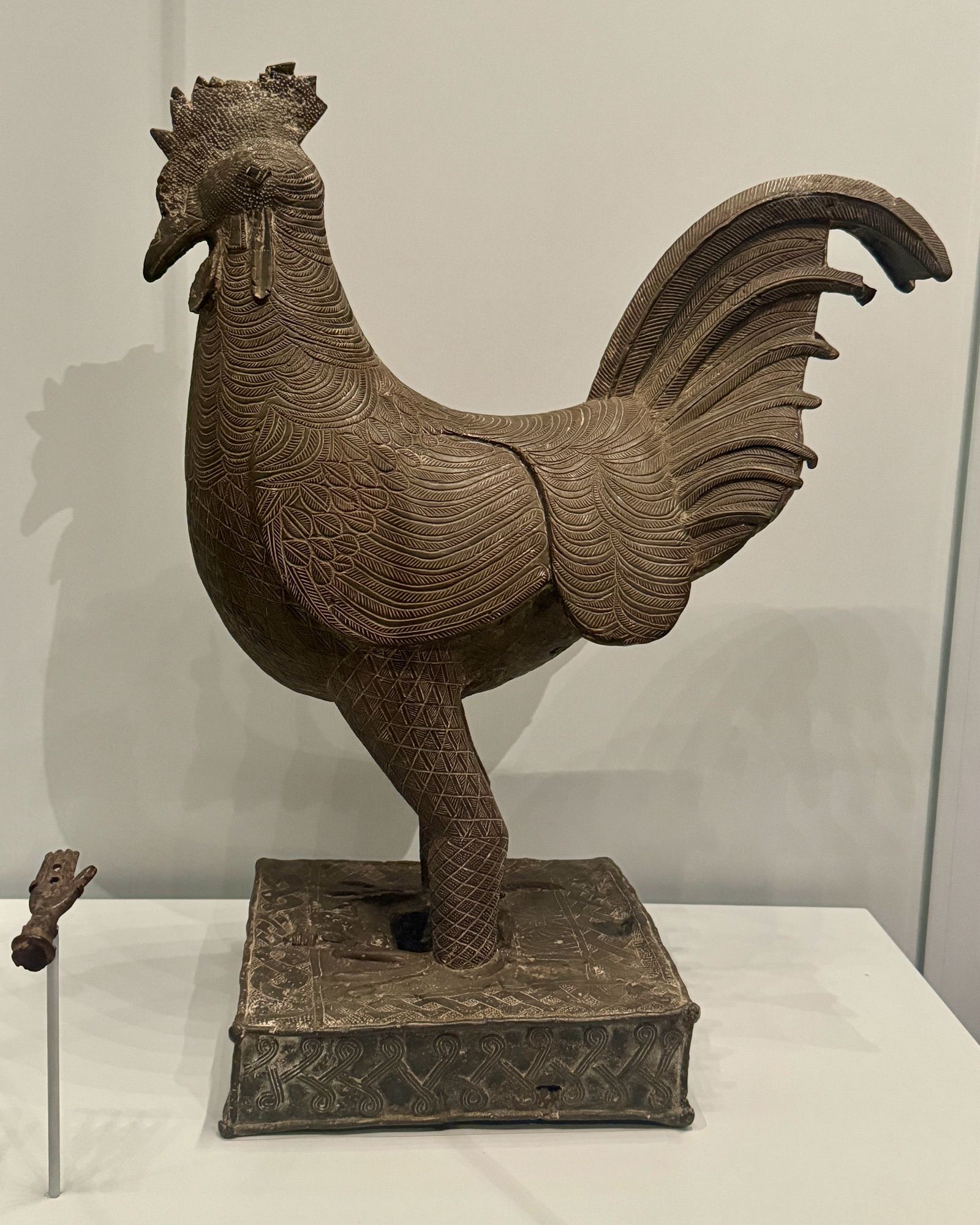 photo of one of the two bronze rooster sculptures in side profile on display at museum