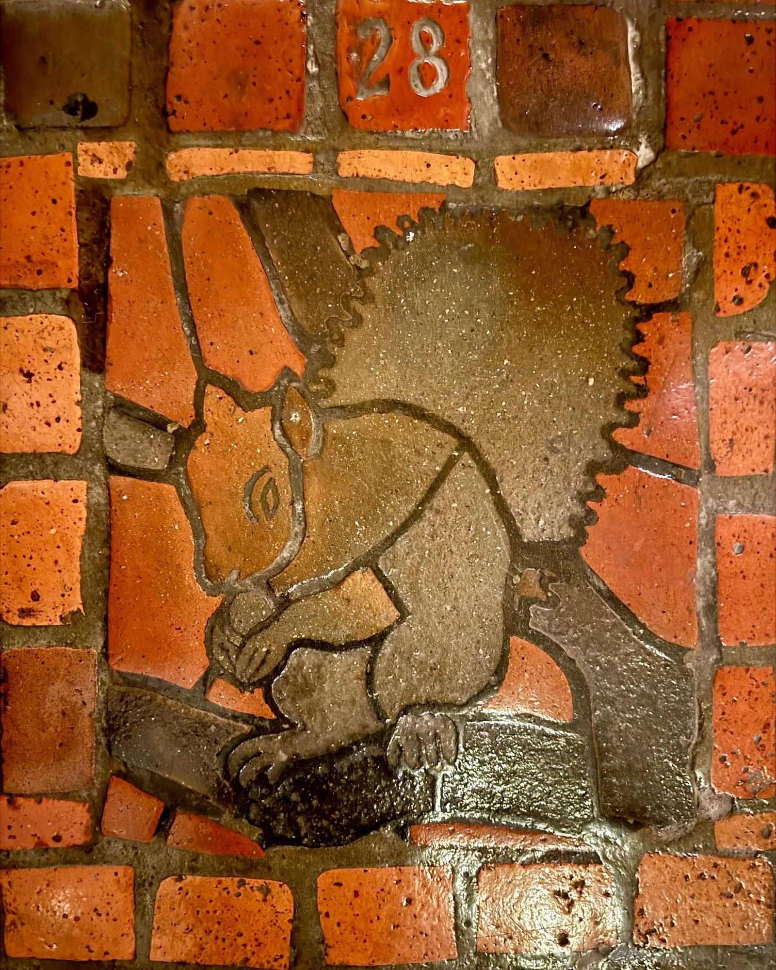 photo of one of the four versions of the grey squirrel floor tile mosaic on the PA Capitol floor, all depicting  squirrel eating a nut on a tree branch: this one numbered “28”