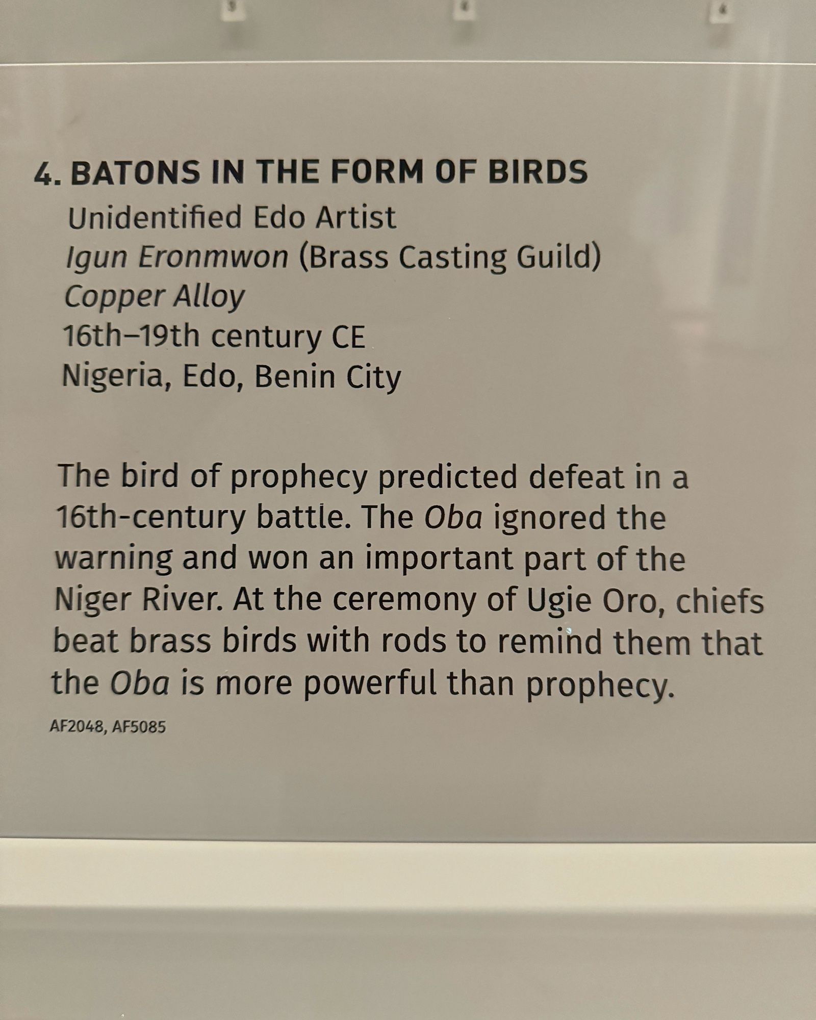 photo of the gallery label:
“4. BATONS IN THE FORM OF BIRDS
Unidentified Edo Artist
Igun Eronmwon (Brass Casting Guild)
Copper Alloy
16th-19th century CE
Nigeria, Edo, Benin City
The bird of prophecy predicted defeat in a 16th-century battle. The Oba ignored the warning and won an important part of the Niger River. At the ceremony of Ugie Oro, chiefs beat brass birds with rods to remind them that the Oba is more powerful than prophecy.
AF2048, AF5085”