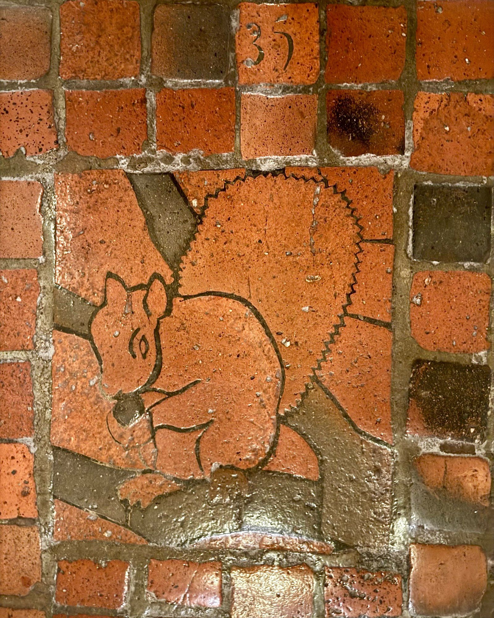 photo of one of the four versions of the grey squirrel floor tile mosaic on the PA Capitol floor, all depicting  squirrel eating a nut on a tree branch: this one numbered “35” and with the squirrel red instead of grey