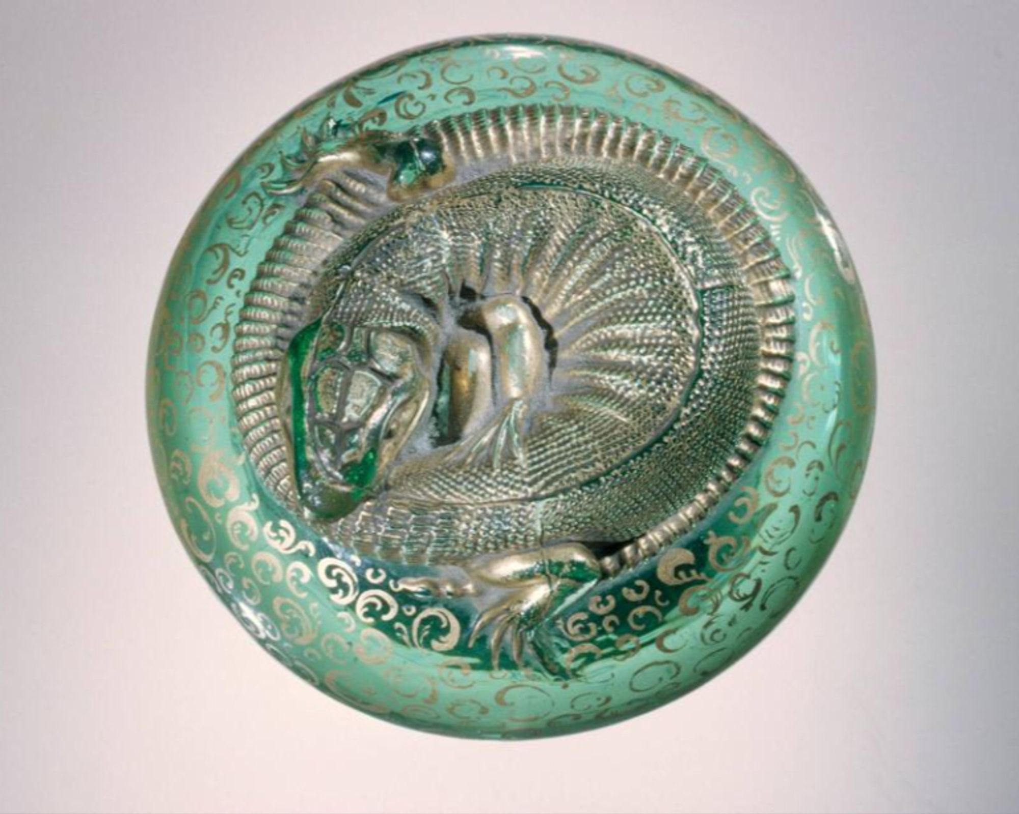 official museum photo of lizard paperweight #1 on light grey background: sea green glass with silver ornamentation, topped with curled up silver lizard
H 6.3 cm, Diam 9 cm