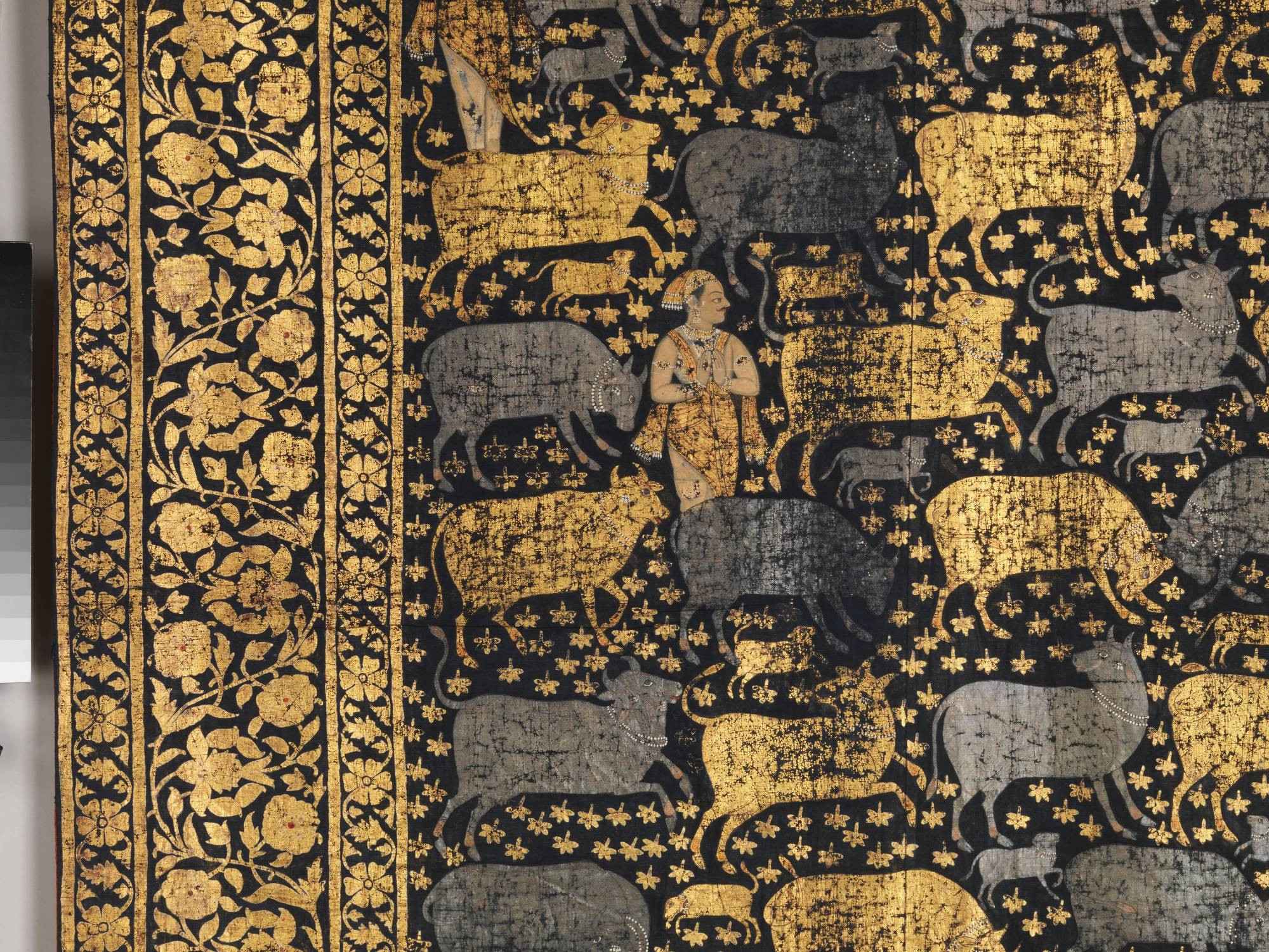 closeup of the textile design showing the ornamental border and primary design of a herder surrounded by gold and silver cows