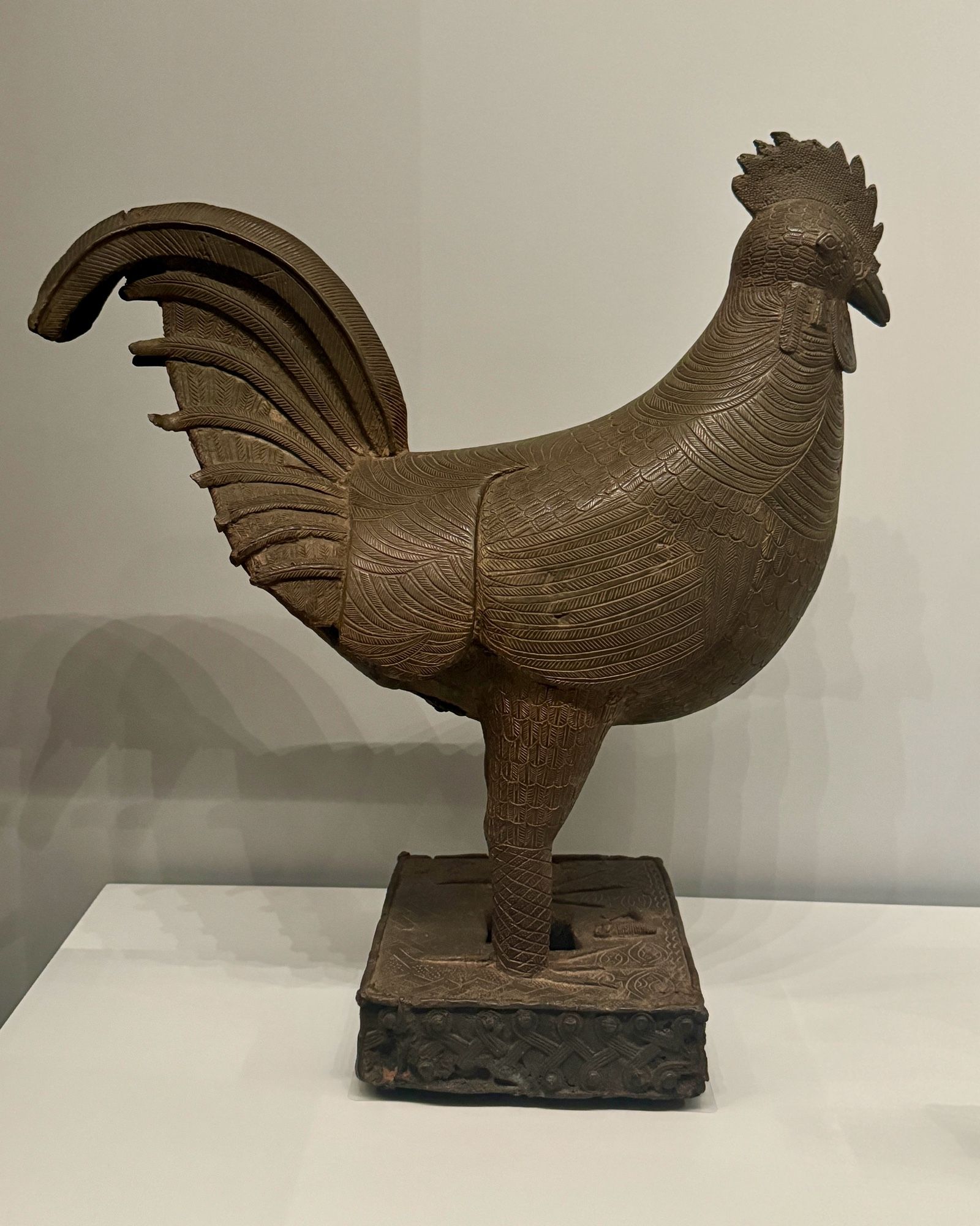 photo of one of the two bronze rooster sculptures in side profile on display at museum