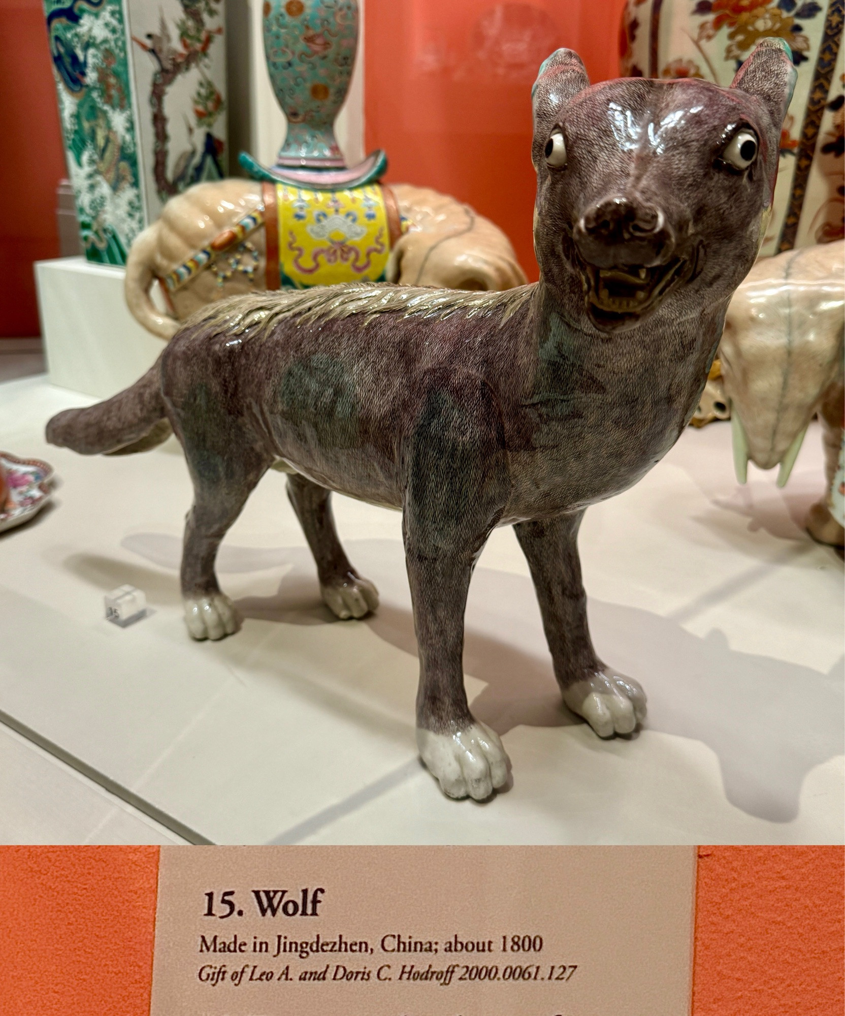 composite photo of the wolf sculpture in front/side profile on display (top) and gallery label (bottom)
Label text:
“15. Wolf
Made in Jingdezhen, China; about 1800
Gift of Leo A. and Doris C. Hodroff 2000.0061.127”