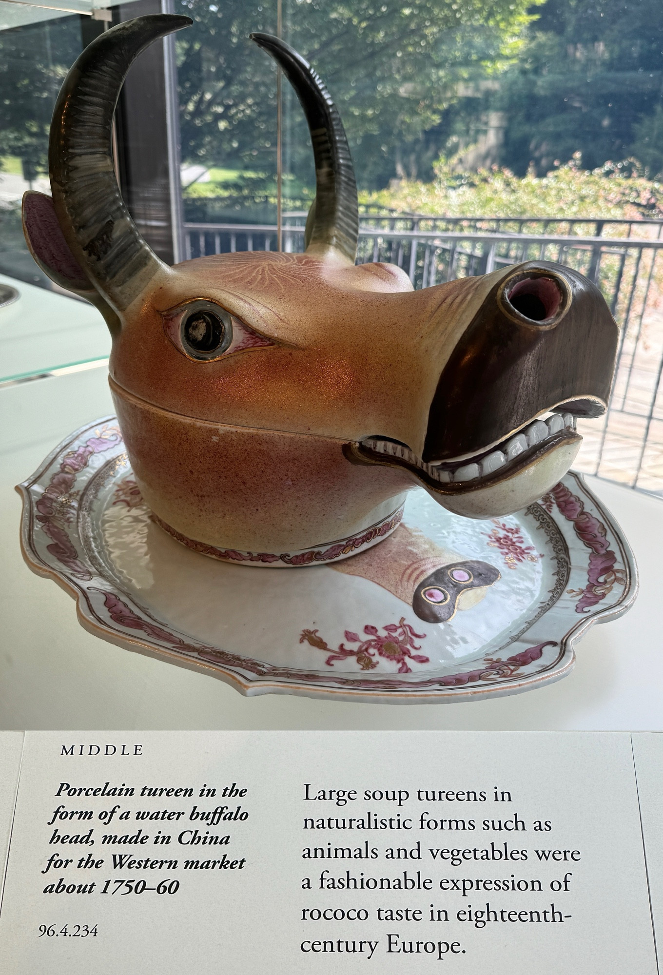 photo of the tureen on display at museum with its gallery label
label text:
“MIDDLE
Porcelain tureen in the form of a water buffalo head, made in China for the Western market about 1750-60
96.4.234
Large soup tureens in naturalistic forms such as animals and vegetables were a fashionable expression of rococo taste in eighteenth-century Europe.”