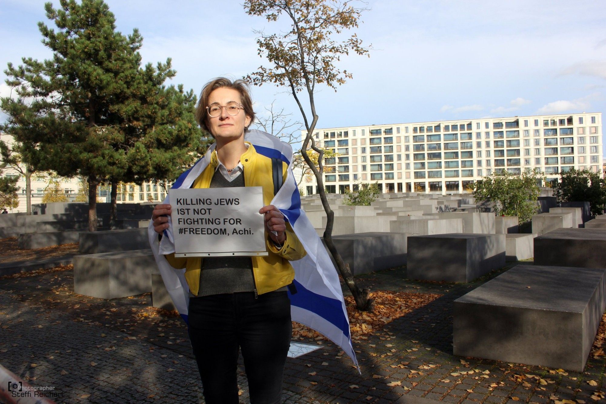 Karolin Preisler (FDP) steht umhangen mit einer Israel Flagge auf dem Holocaust Mahnmal. In ihren Händen hält sie ein Plakat, auf dem steht: "Killing Jews is Not Fighting for Freedom, Achi".