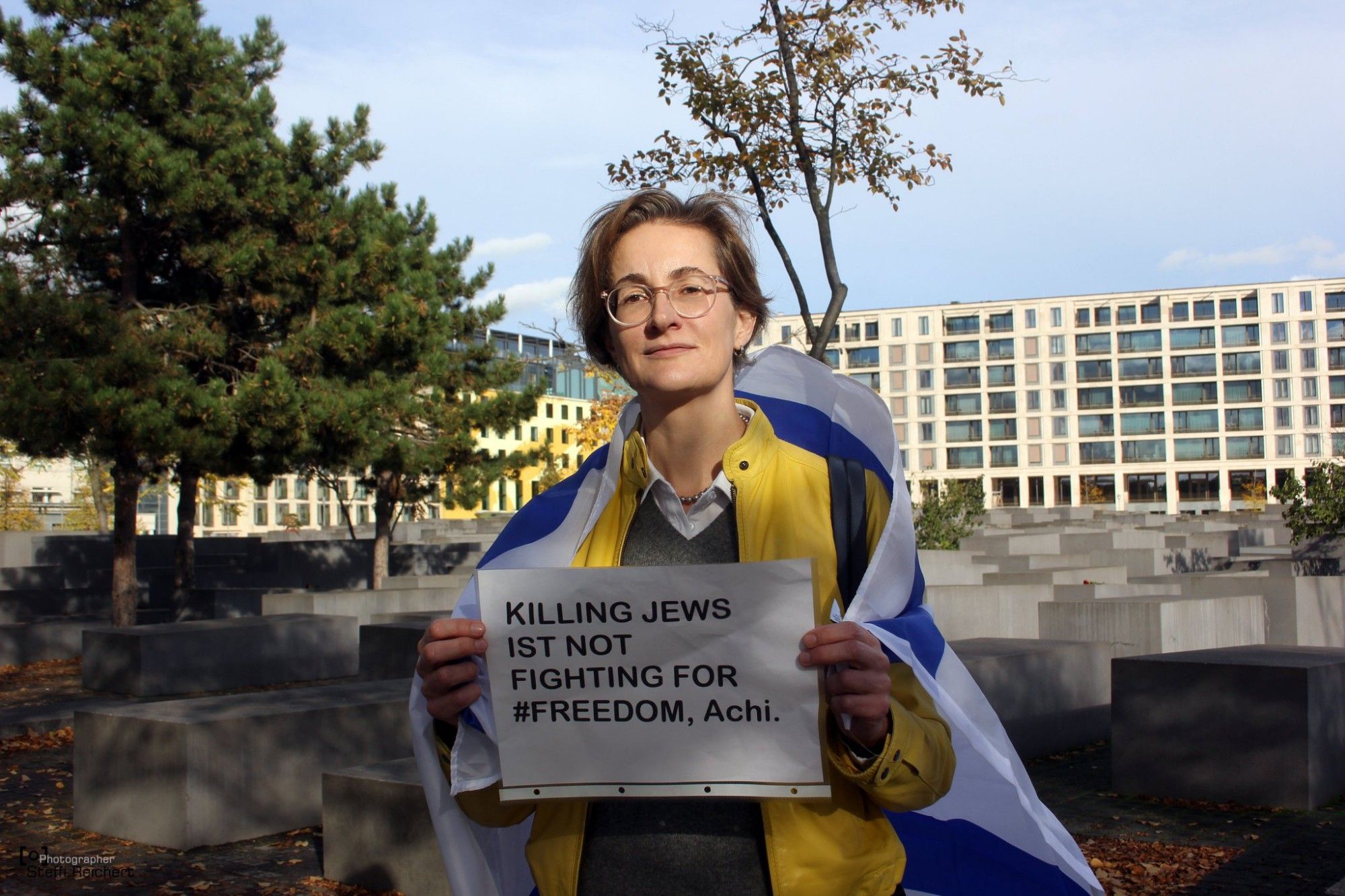 Karolin Preisler (FDP) steht umhangen mit einer Israel Flagge auf dem Holocaust Mahnmal. In ihren Händen hält sie ein Plakat, auf dem steht: "Killing Jews is Not Fighting for Freedom, Achi".